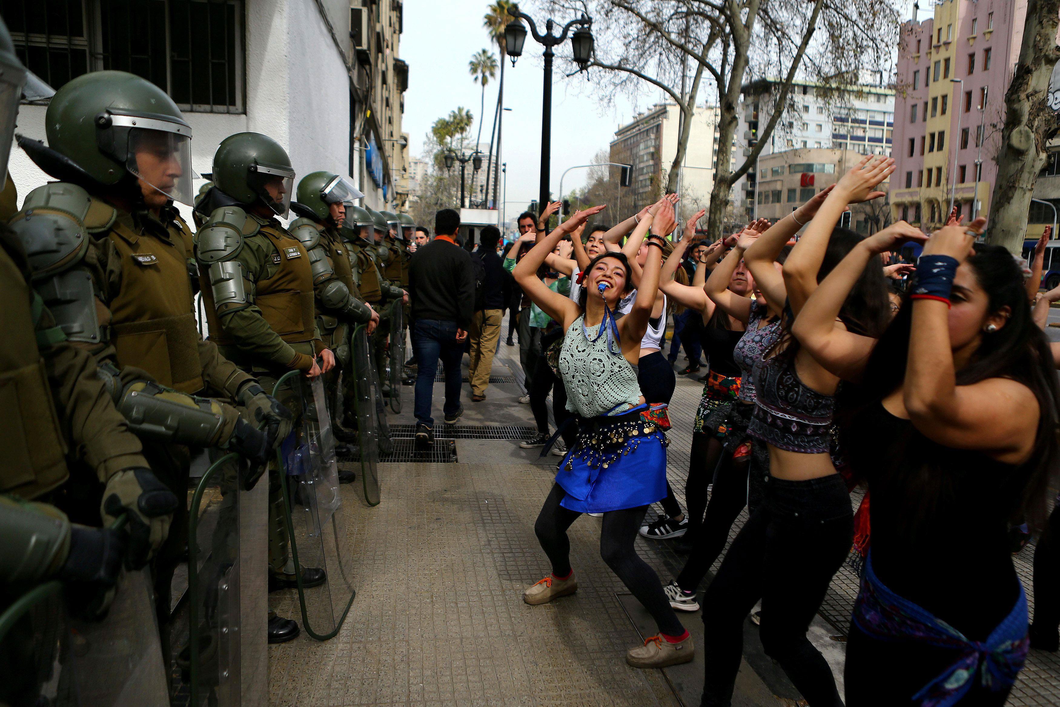 Demonstrators perform a dance in front of riot policemen during a march called by students to reques
