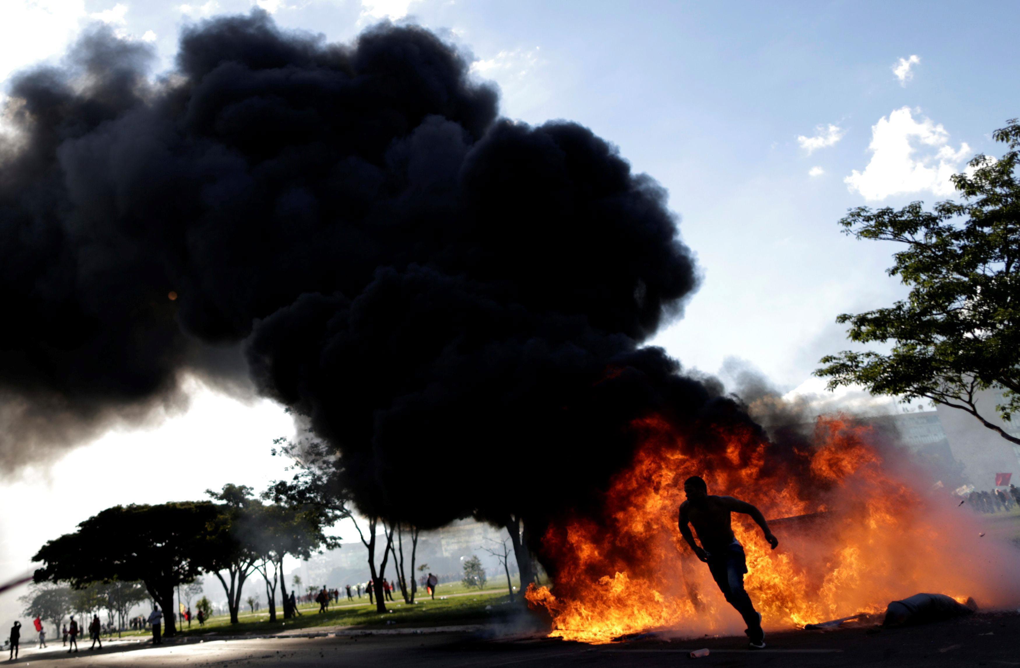 A demonstrator runs near a burning barricade during a protest against President Michel Temer and the