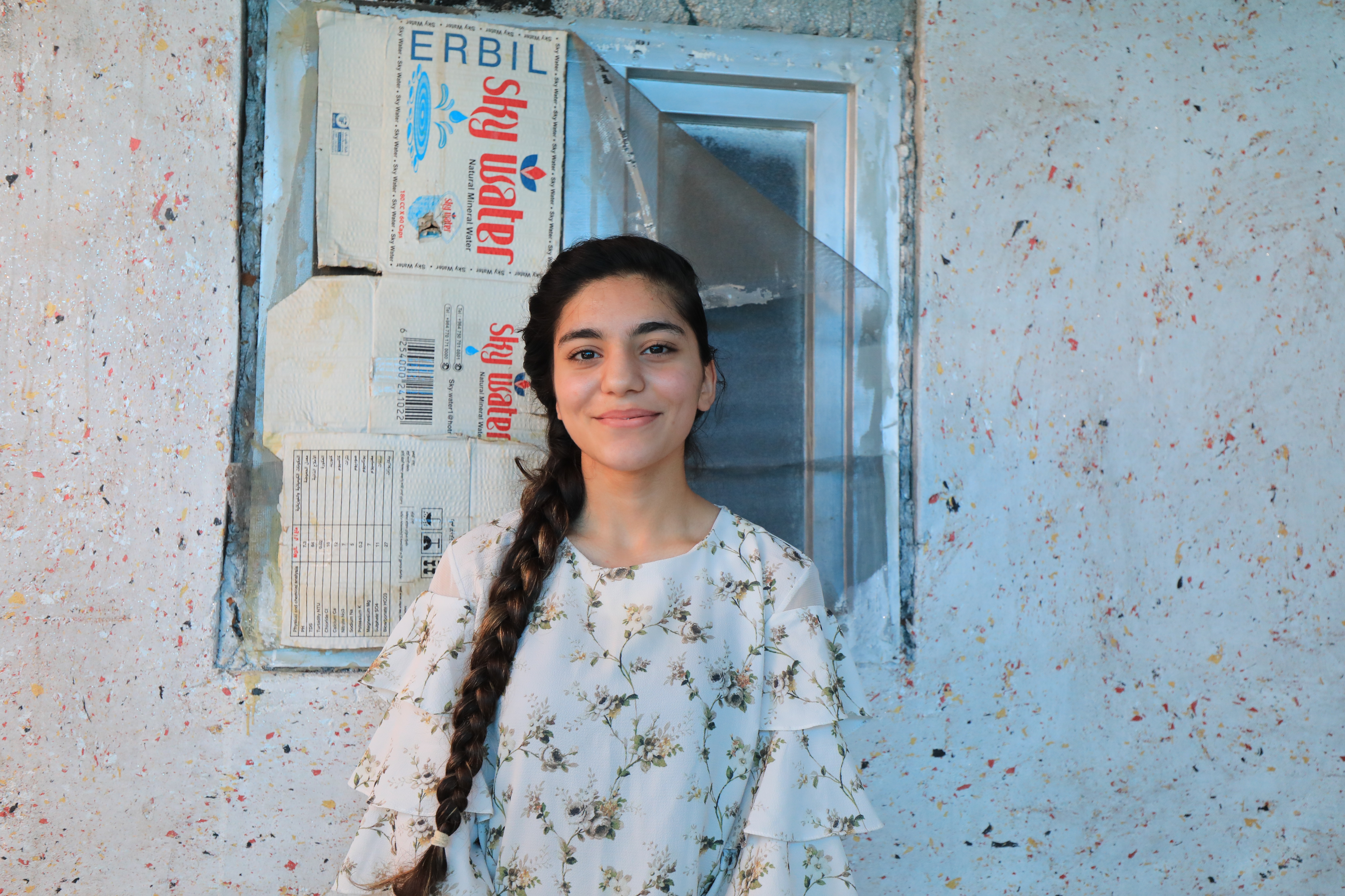 Qushtapa. Peyman ma 17 lat. Jest Kurdyjką z Syrii. Imię, które nosi oznacza w „zgoda” albo „obietnica’. „Zgoda” pasuje lepiej, bo Peyman dziewczyna pogodziła się ze swym wyjątkowo podłym losem. W obozie mieszka wraz z matką – to ona ją utrzymuje. Pracuje od czternastego roku życia. Ostatnio w fabryce jogurtu w sąsiednim mieście. Praca zajmuje jej po 8-10 godzin dziennie plus dojazdy, nie ma więc czasu by się uczyć. Zresztą nawet gdyby poszła do szkoły, to musiałaby zacząć od zera, bo ledwie duka po arabsku, zaś w języku kurdyjskim, którego naucza się w obozowej szkole, tylko mówi. Peyman straciła ojca i dwie siostry, z których jedna była jej bliźniaczką, podczas ucieczki z Efrin do Aleppo. Rodzina została po prostu brutalnie rozdzielona przez żołnierzy. Peyman nie pamięta, czy byłą to armia Assada czy rebelianci. Po ojcu słuch zaginął – najpewniej został zabity. Siostry spotkał lepszy los. Jedna odnalazła się po latach w USA – okazało się, że zaadoptowała ją jakaś amerykańska rodzina. Druga odezwała się z Niemiec, gdzie ściągnął ją w ramach łączenia rodzin poślubiony w międzyczasie Kurd. Peyman utrzymuje kontakt z sistrami za pomocą mediów społecznościowych. Bardzo chciałaby się z nimi zobaczyć, ale jedynym dokumentem jaki posiada, jest syryjski aktu urodzenia. To za mało, by dostać nawet prawo do pobytu w Iraku, nie mówiąc już o paszporcie czy zagranicznej wizie.