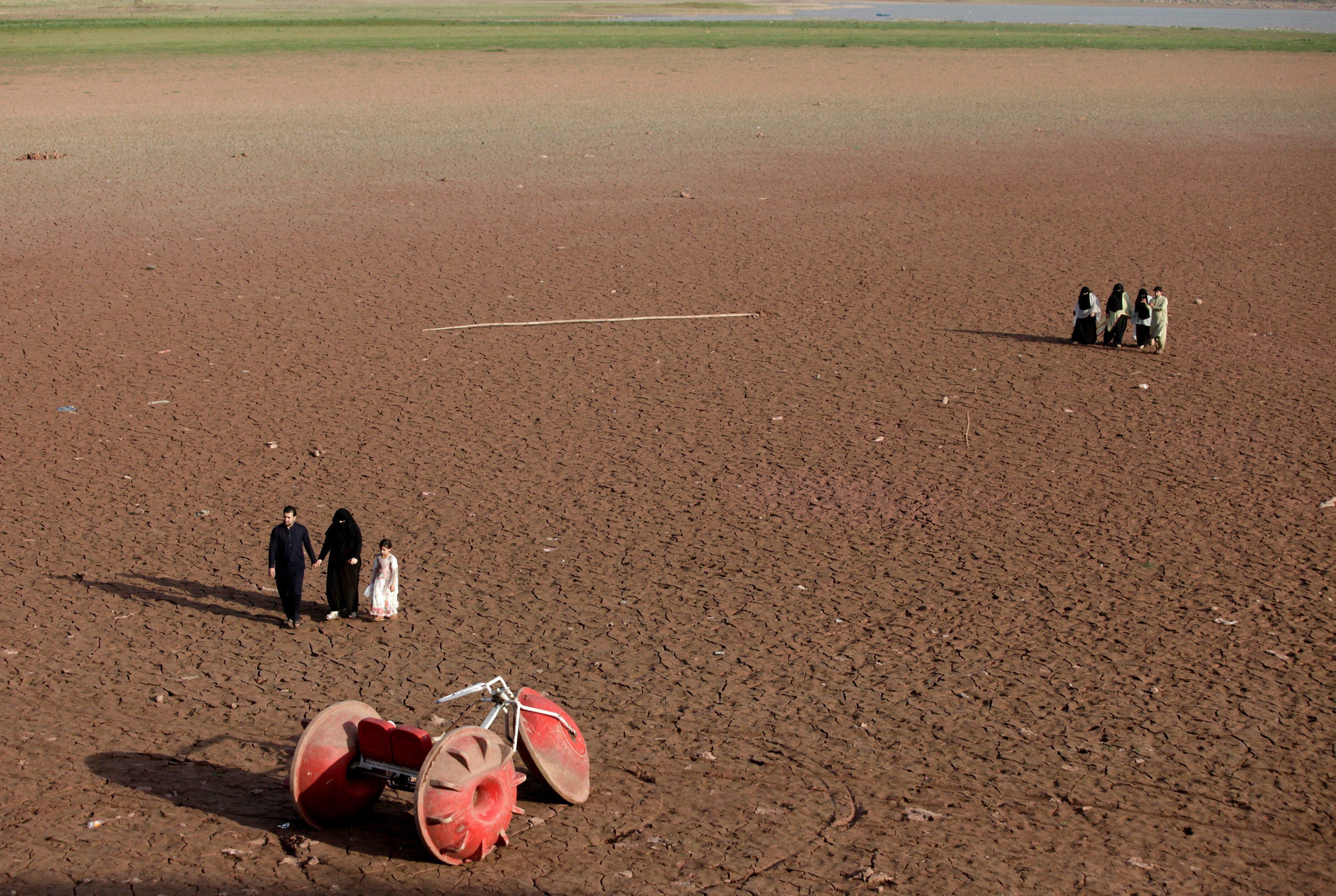 People walk near a three-wheeler parked at a dry portion of land that used to have water, at the ban