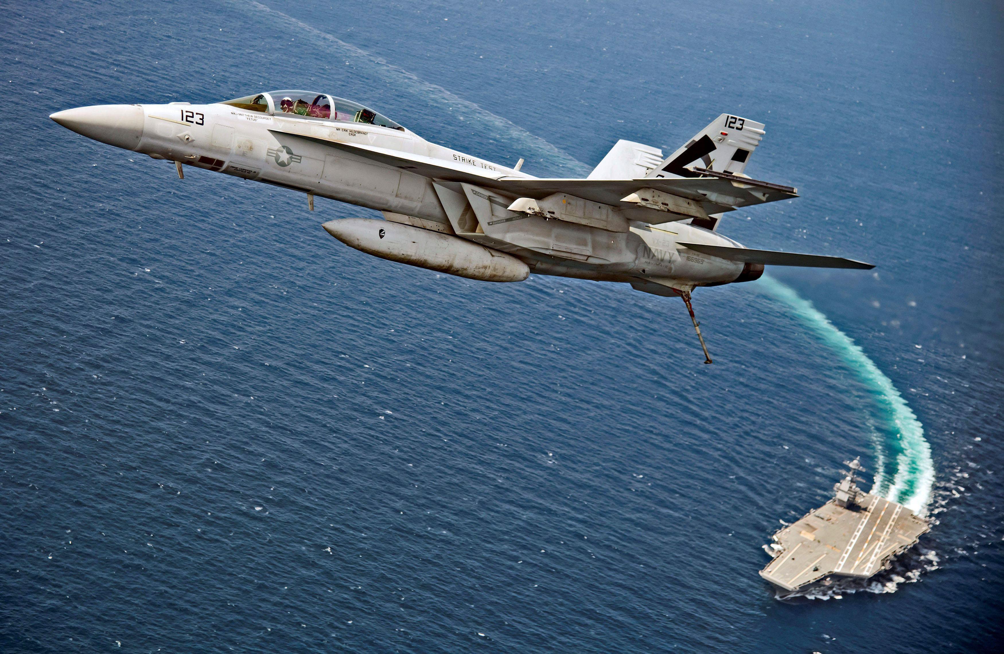 An F/A-18F Super Hornet jet flies over the USS Gerald R. Ford as the U.S. Navy aircraft carrier test