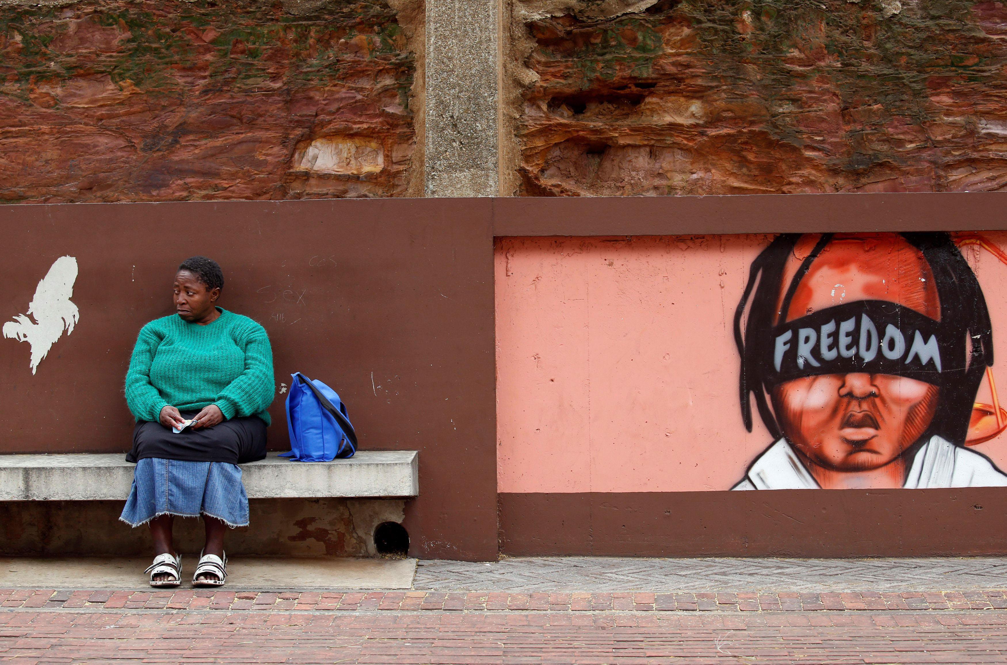 A woman sits next to murals as opposition parties march for the removal of President Jacob Zuma outs