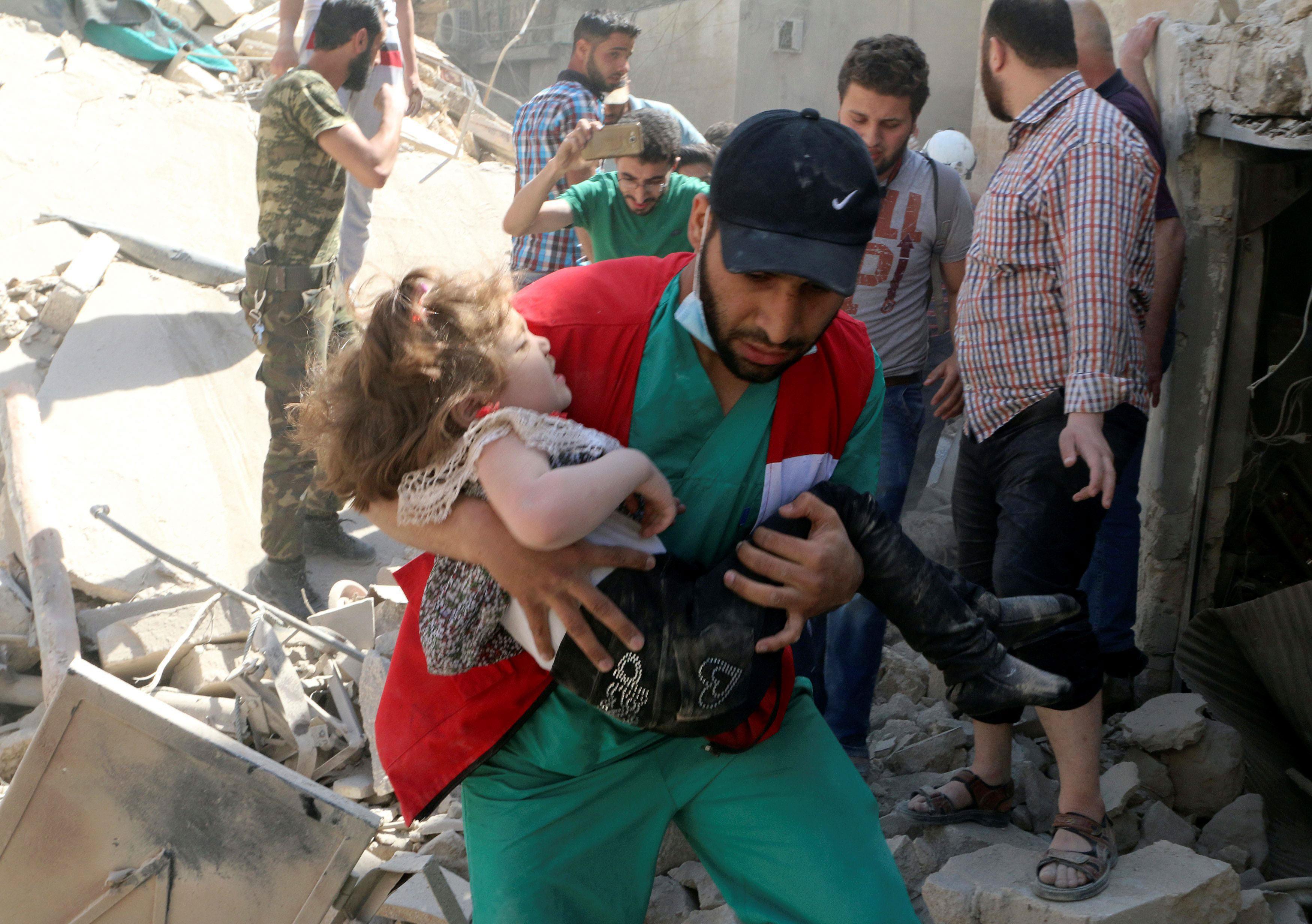 A civil defence member carries a child that survived from under the rubble at a site hit by airstrik