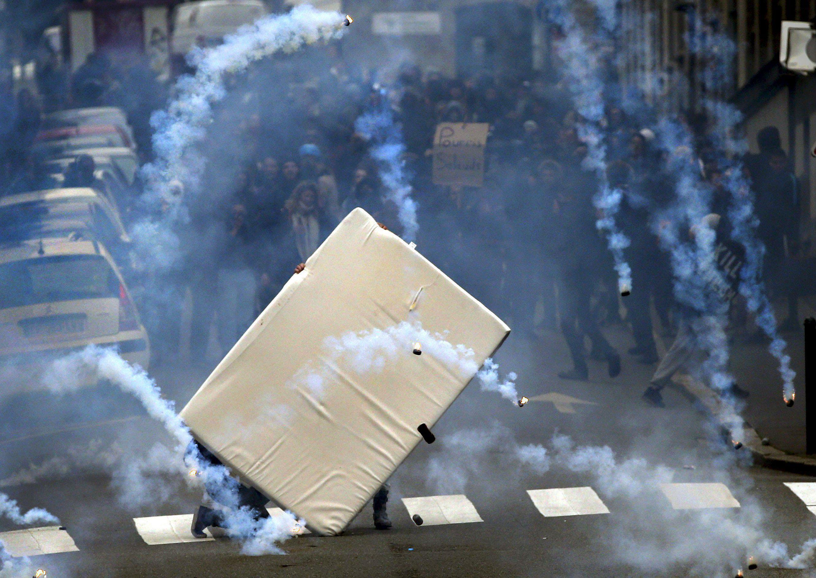 Youths take cover behind a mattress during clashes as French high school and university students att