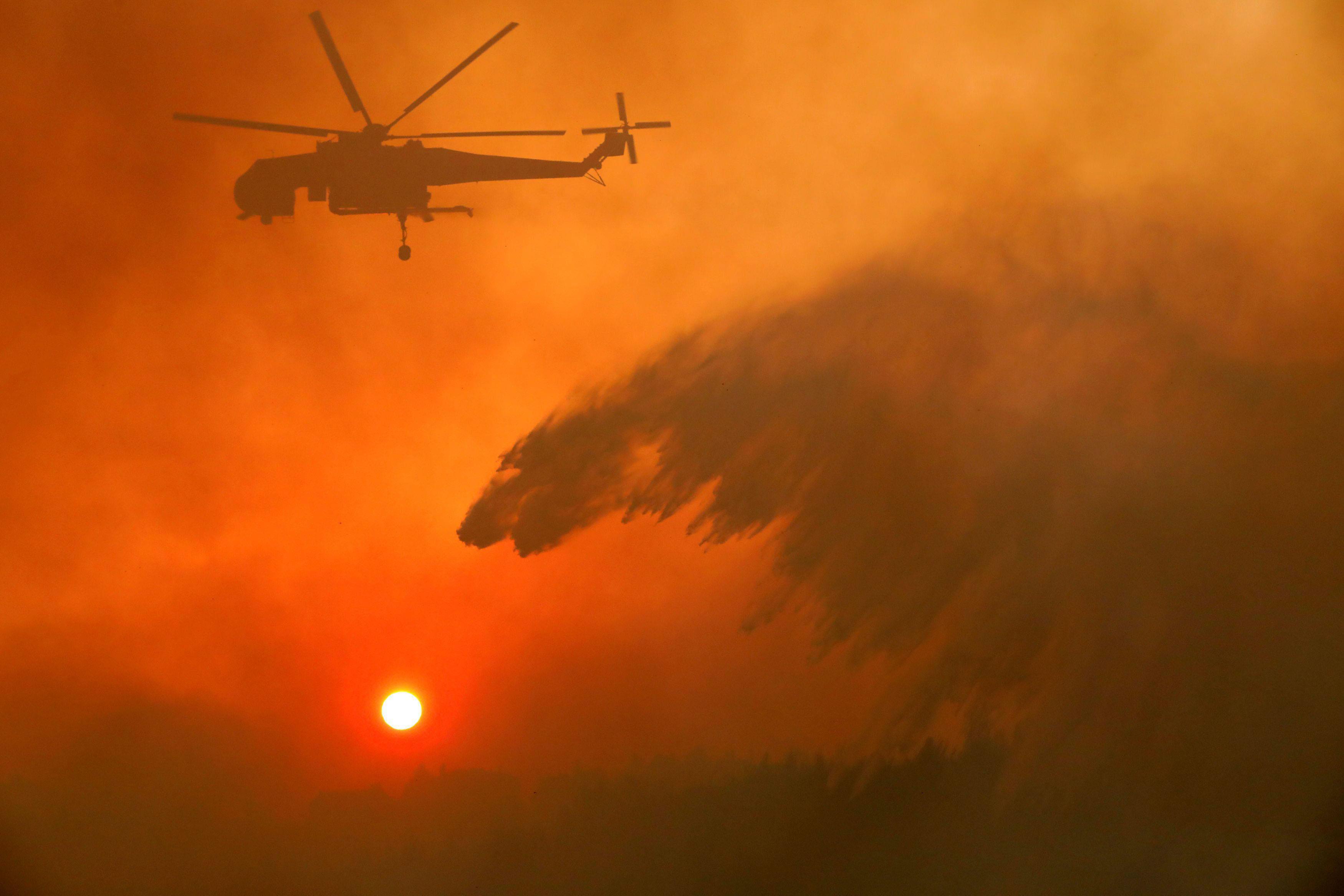 A firefighting helicopter makes water drop as a wildfire burns near the village of Metochi