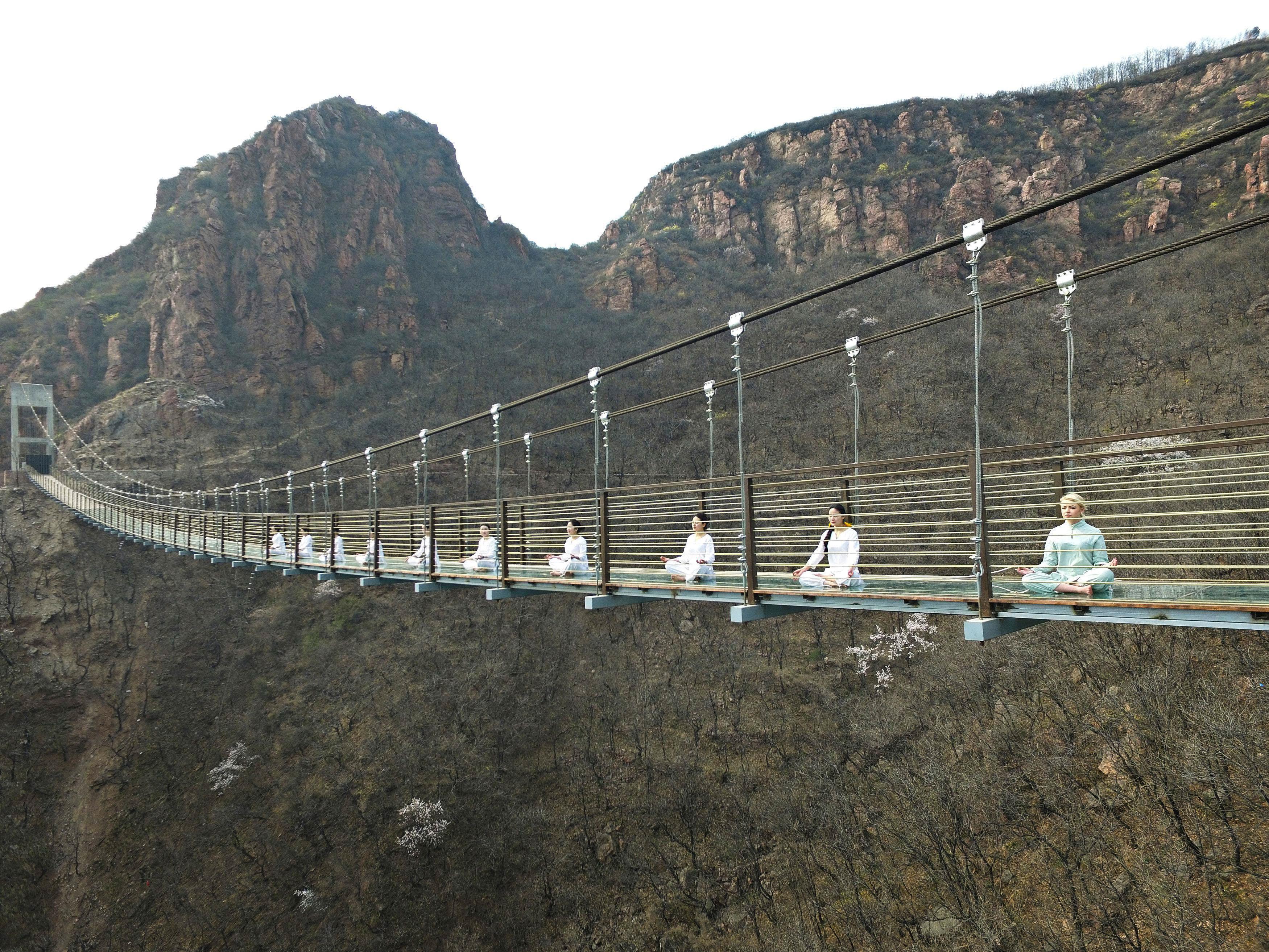 Women perform yoga on a glass suspension bridge as a way to attract tourists in Fuxishan