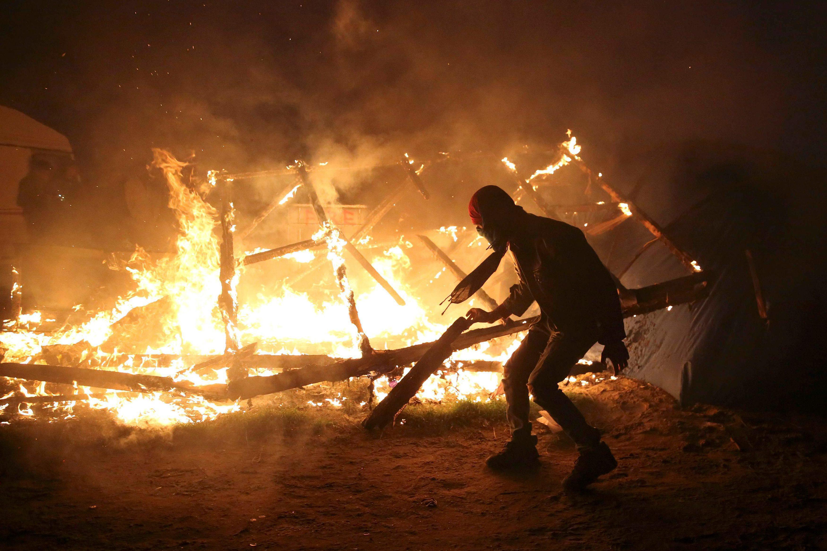 A migrant is seen in silhouette near flames from a burning makeshift shelter on the second day of th