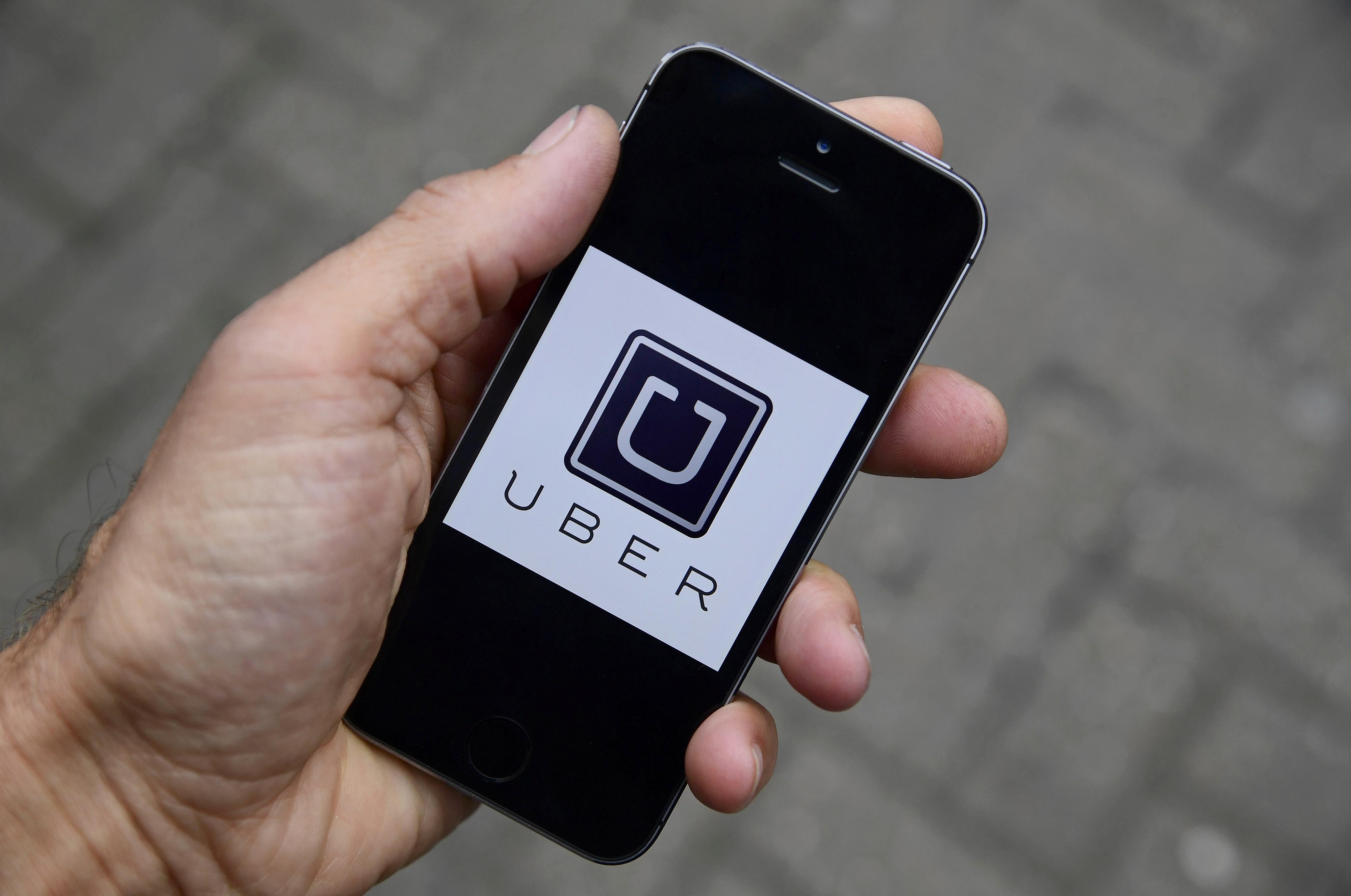 A photo illustration shows the Uber app logo displayed on a mobile telephone, as it is held up for a