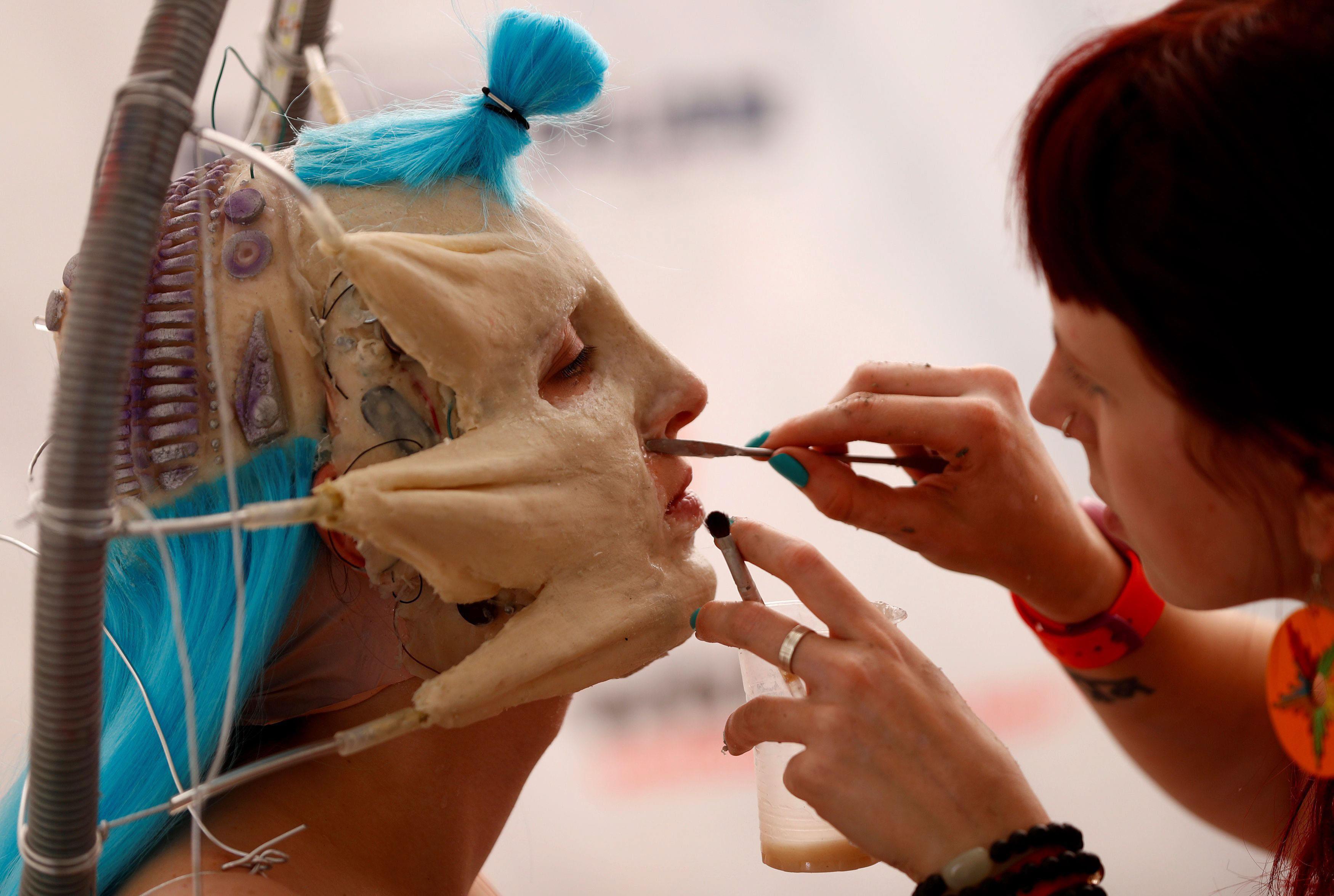 An artist touches up makeup on a model during the 