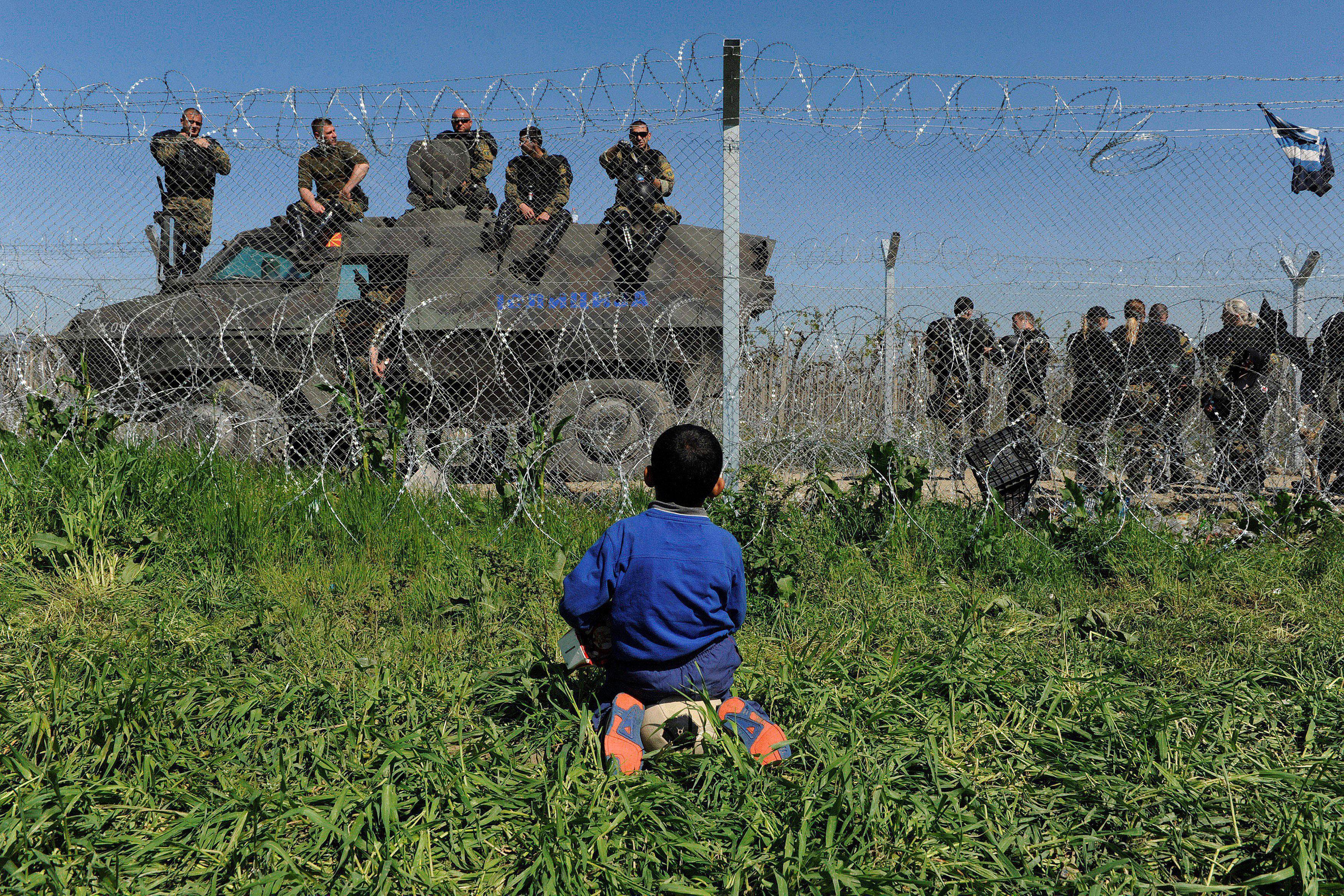 A boy sits on his ball next to a border fence on the Greek side of the border, as Macedonian police 