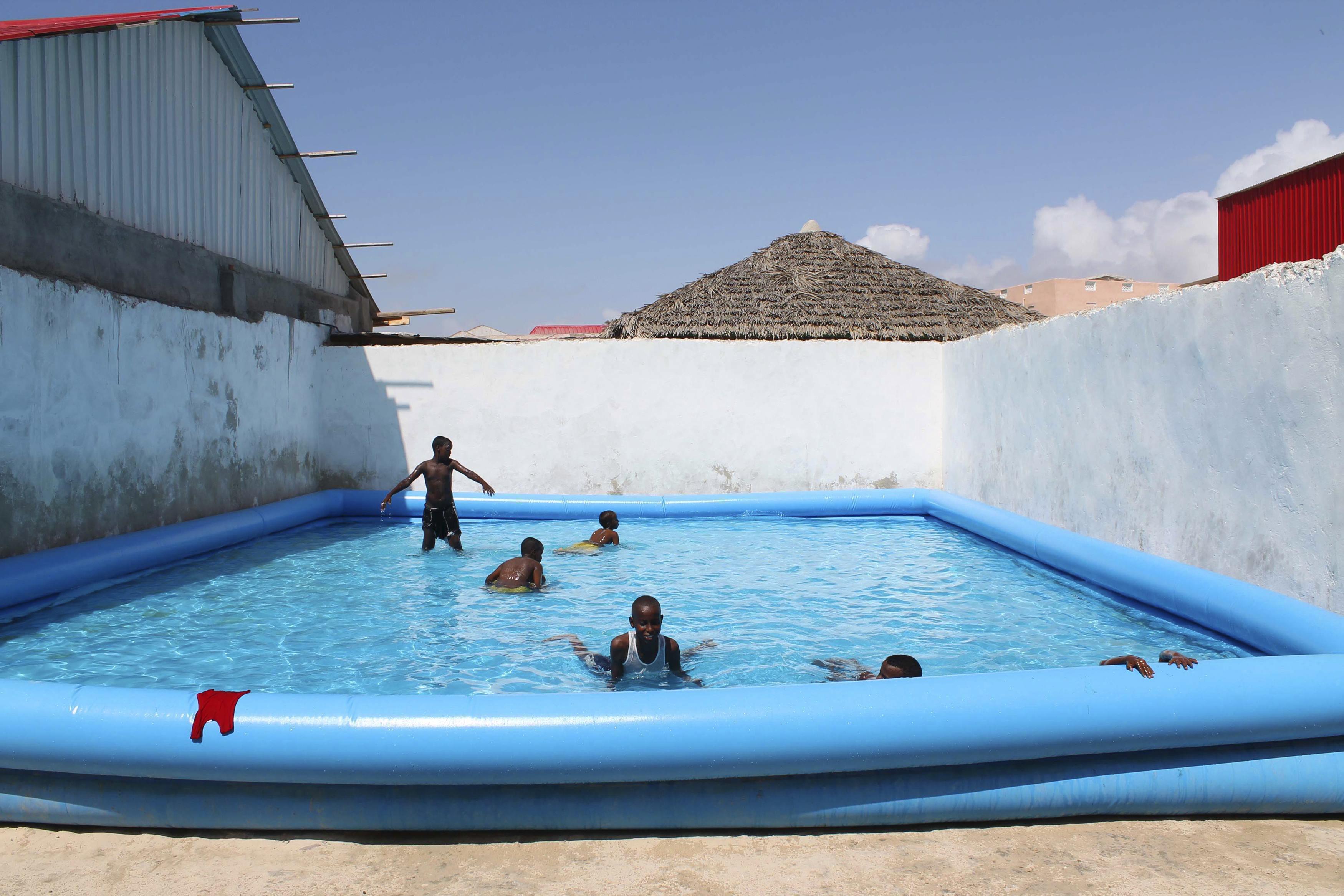 Children play in a swimming pool at a guest hotel in Mogadishu October 16, 2013. Street lamps now br