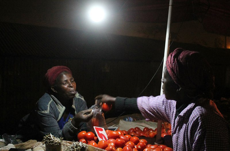 A vegetable vendor selling her wares deep into the night while relying on solar powered bulb to provide light.
