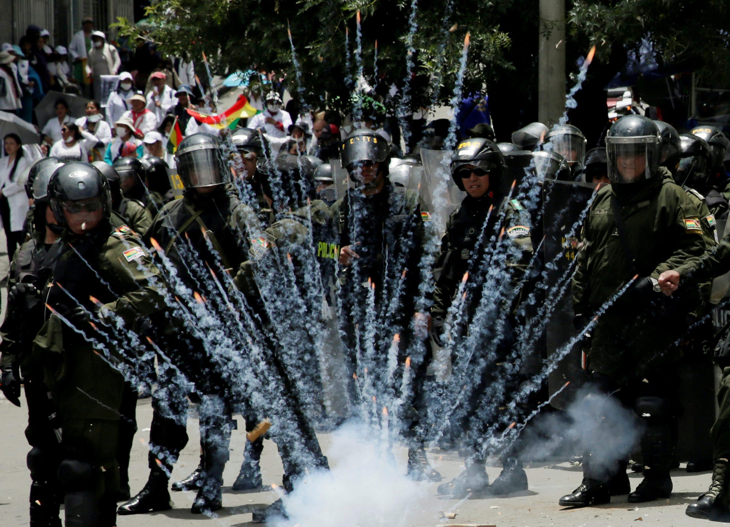 A firecracker explodes next to riot police officers during a protest rally against Bolivia's governm