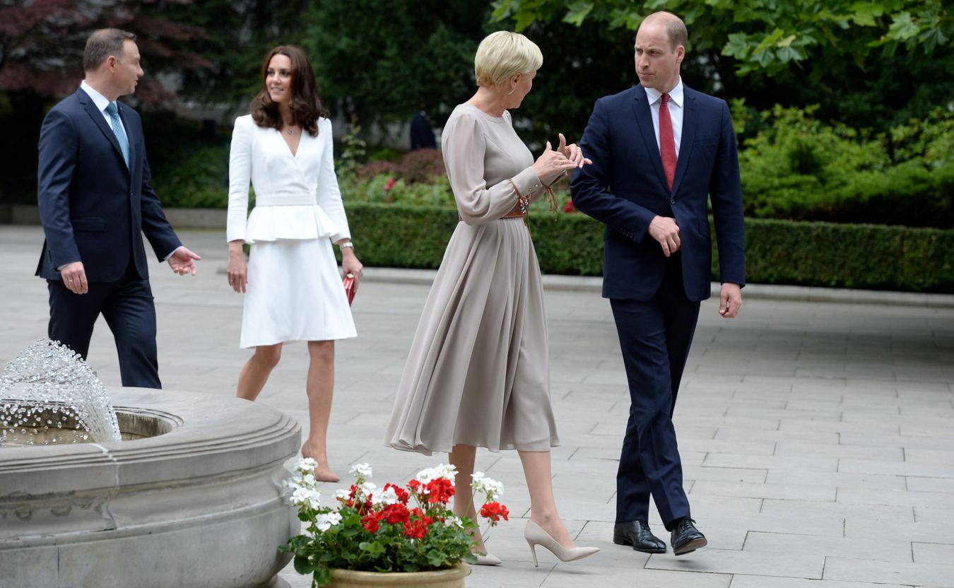 Księżna Kate ubrana jest w biały kostium i cieliste szpilki, William jest w ciemnym garniturze. Polska pierwsza dama jest w długiej sukni w kolorze pudrowego różu.