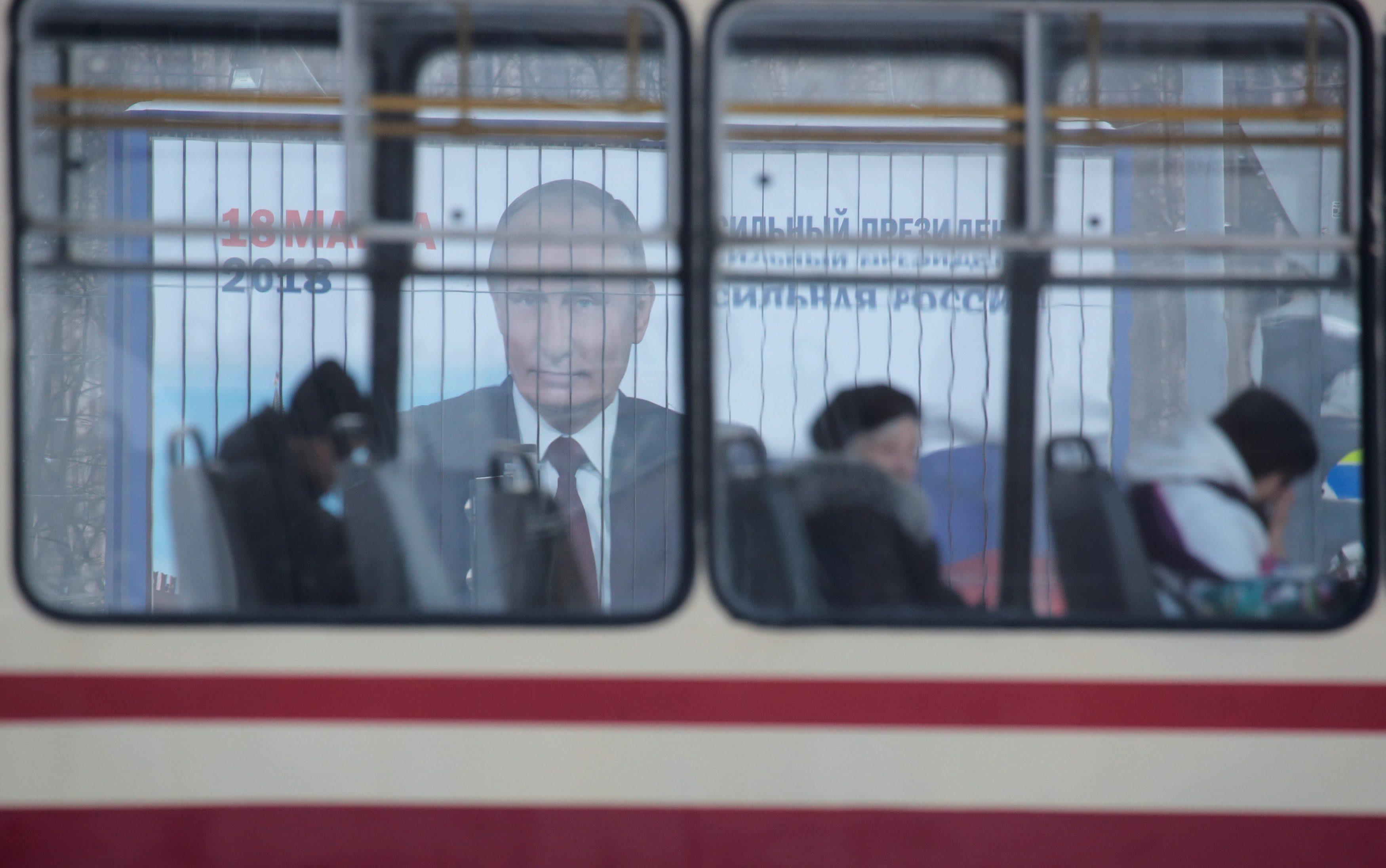 People ride a tram past a board, which advertises the campaign of Russian President Putin ahead of t