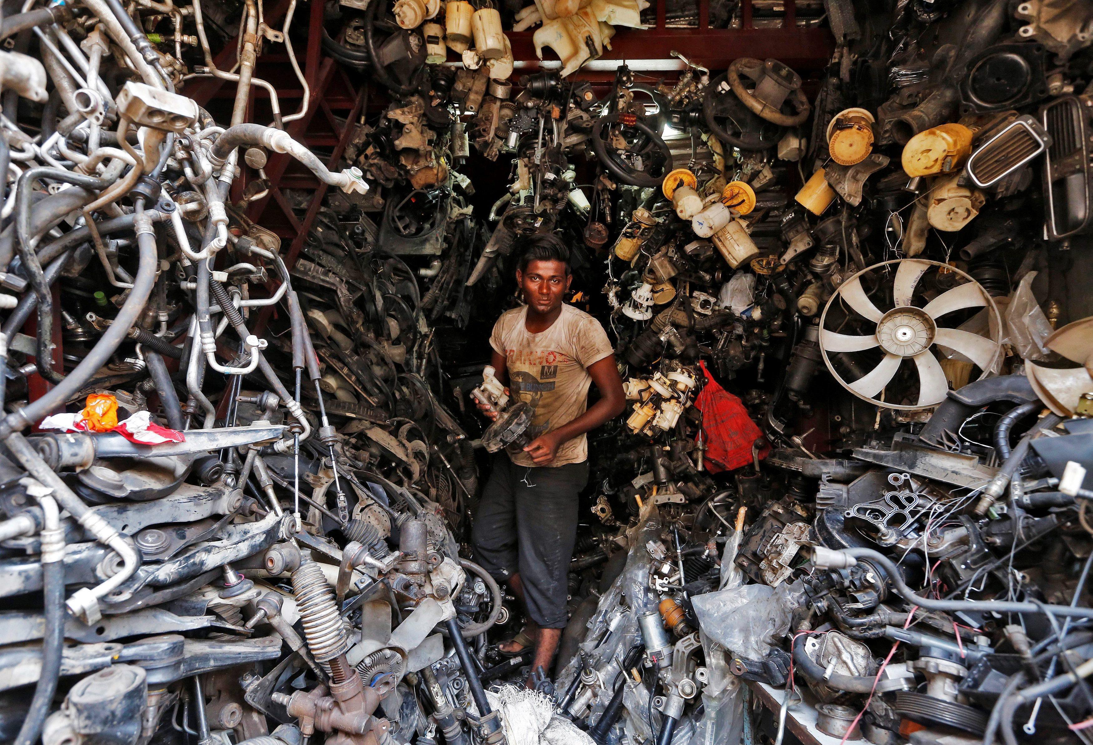 A worker carries a part of a used car inside a shop at a second-hand automobile parts market in Mumb