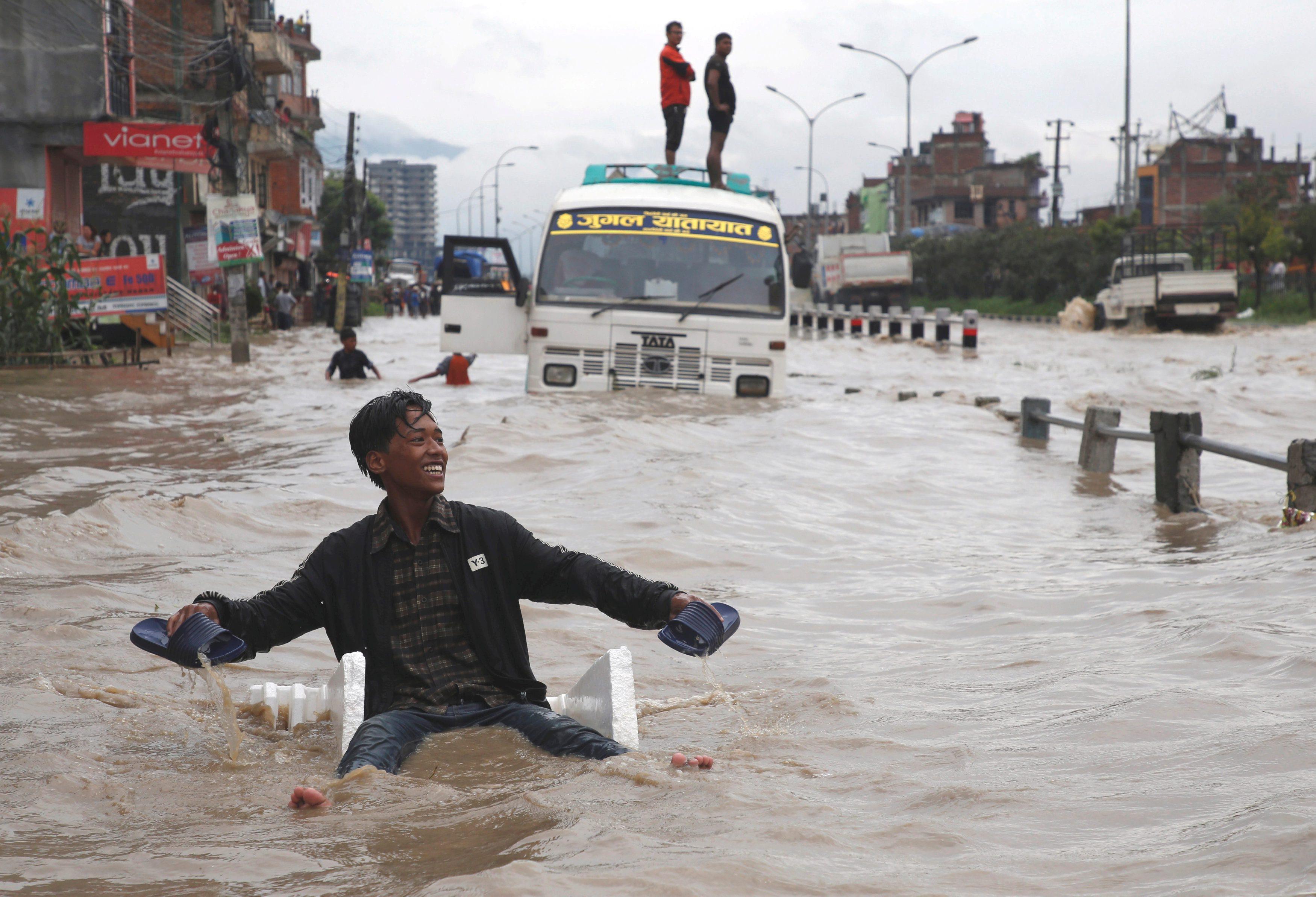 A boy smiles as he uses an improvised raft to maneuver through the floodwater after incessant rainfa