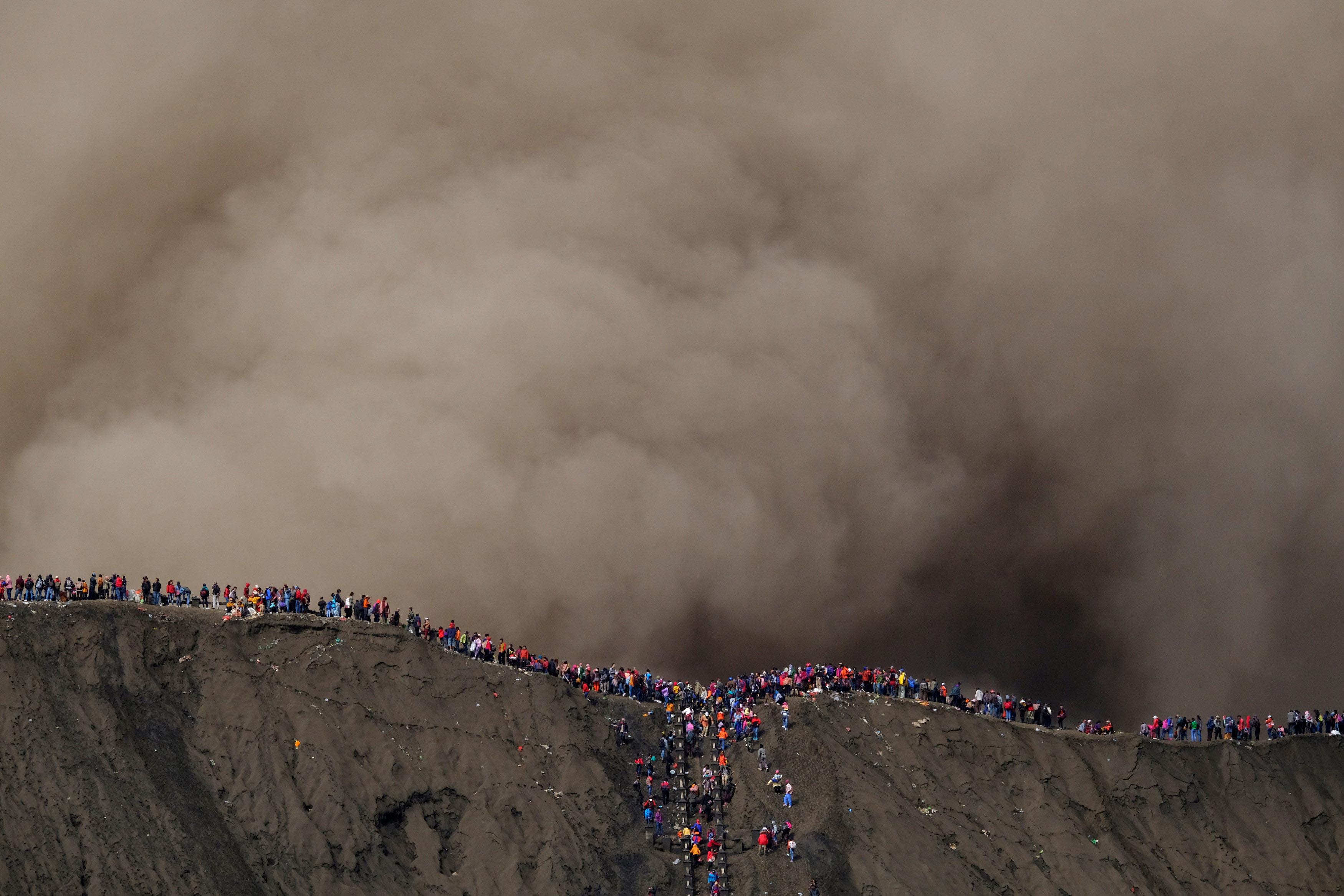 Hindu villagers and visitors stand on the edge of the volcanic crater of Mount Bromo as smoke and as