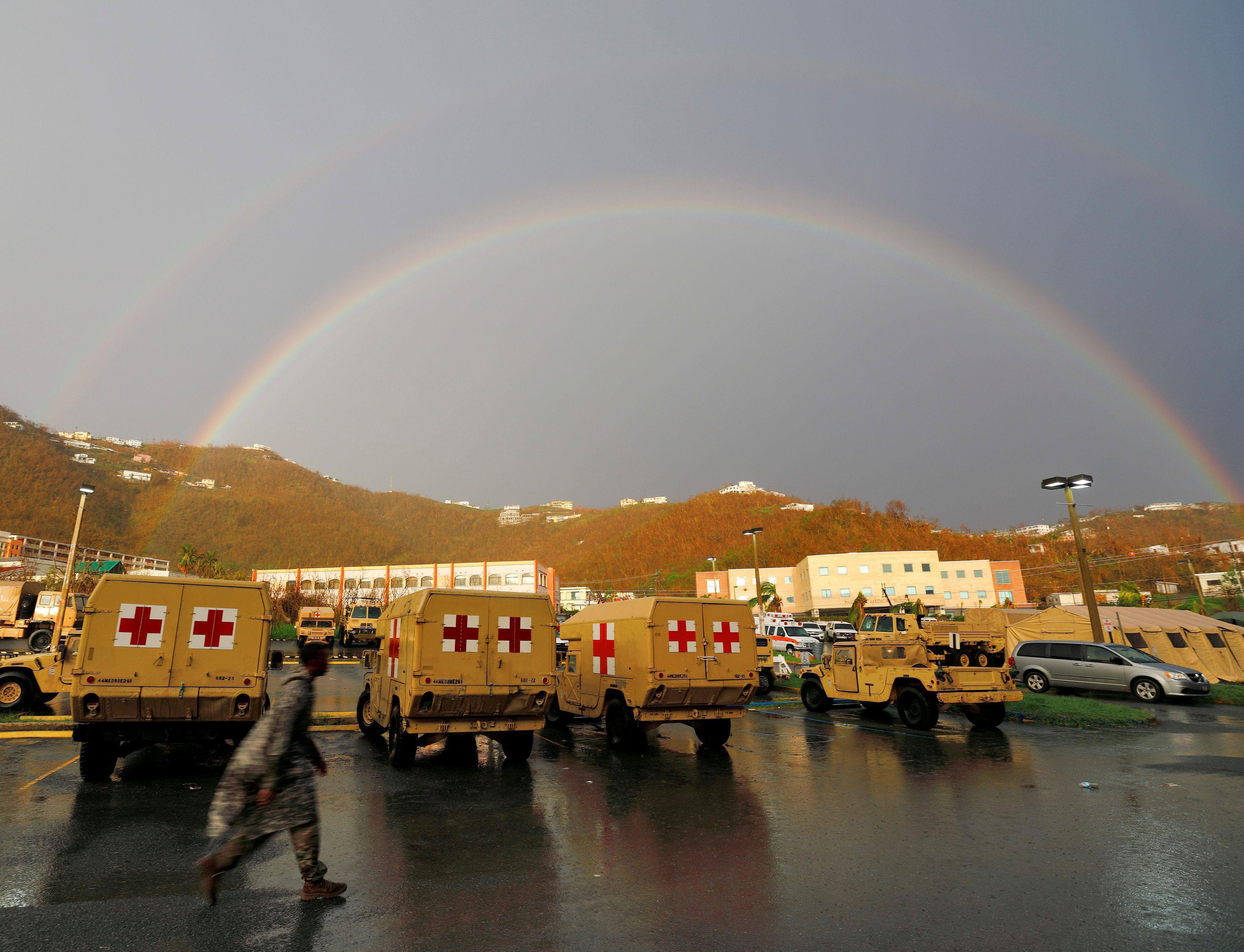 A soldier walks past a row of vehicles while a double rainbow appears in the sky over the U.S. Virgi