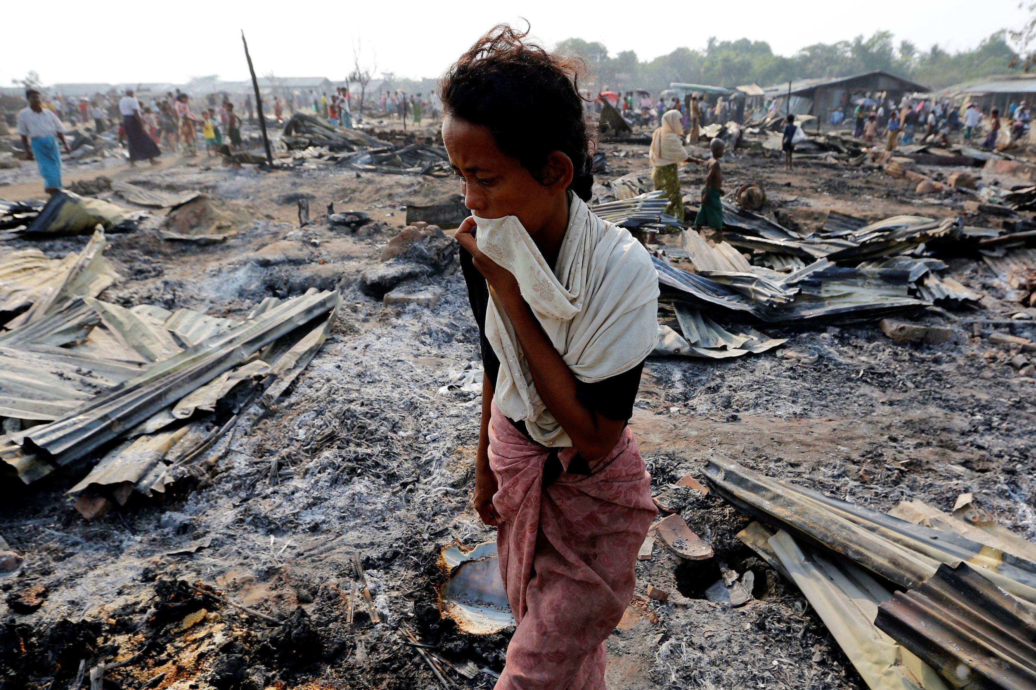 A woman walks among debris after fire destroyed shelters at a camp for internally displaced Rohingya