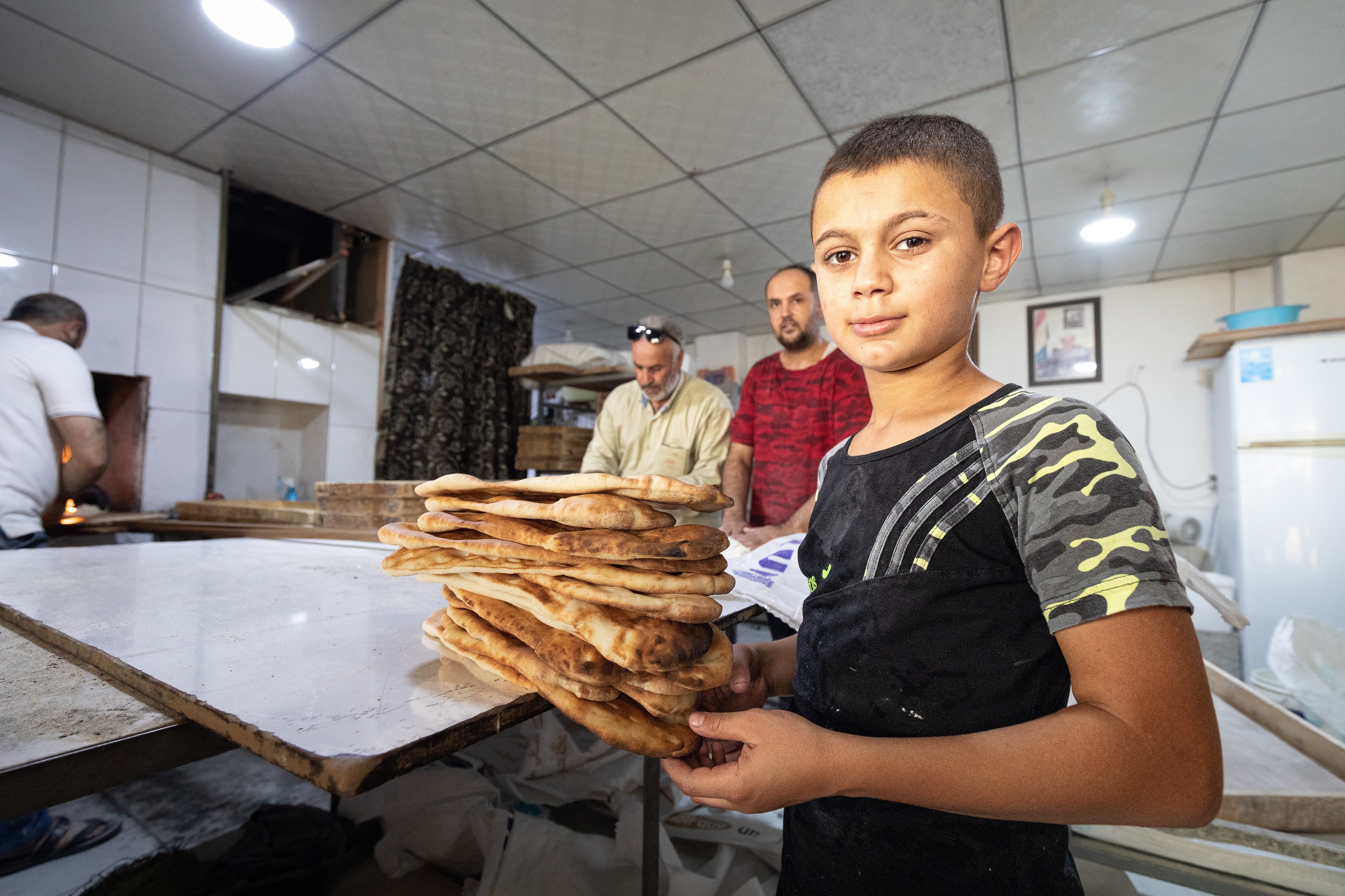 Qushtapa. Muhammad, młodociany pomocnik piekarza, prezentuje świeżo upieczone arabskie chlebki. Chłopak jest dumny z tego, że pomaga rodzinie.