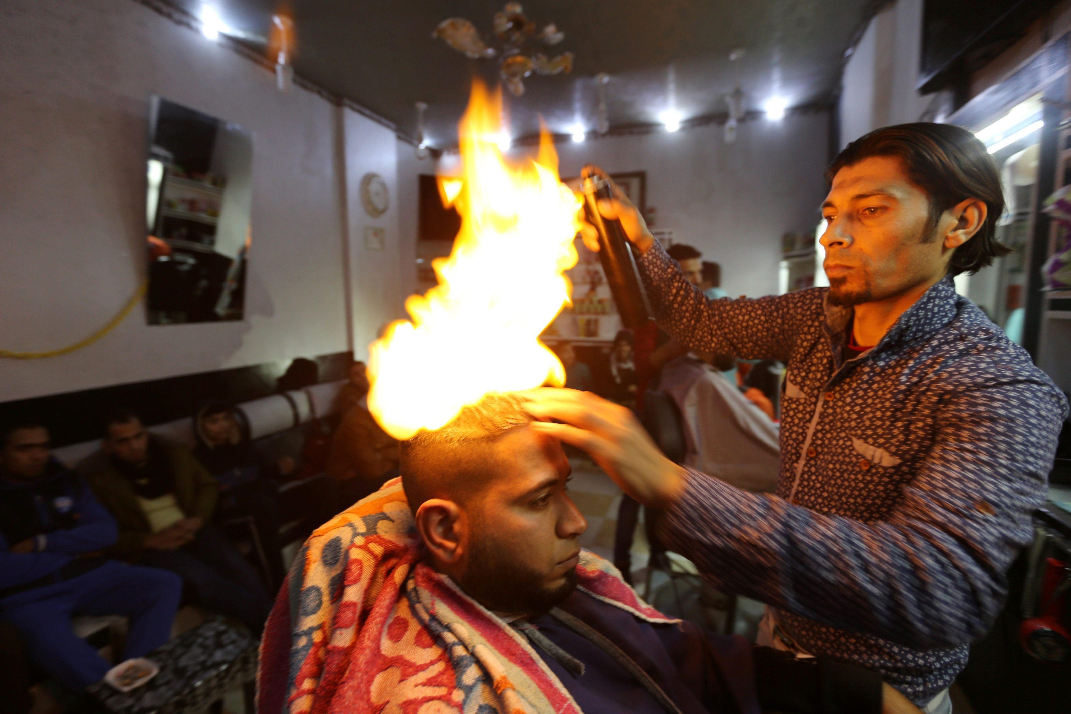 Palestinian barber Ramadan Odwan styles and straightens the hair of a customer with fire at his salo
