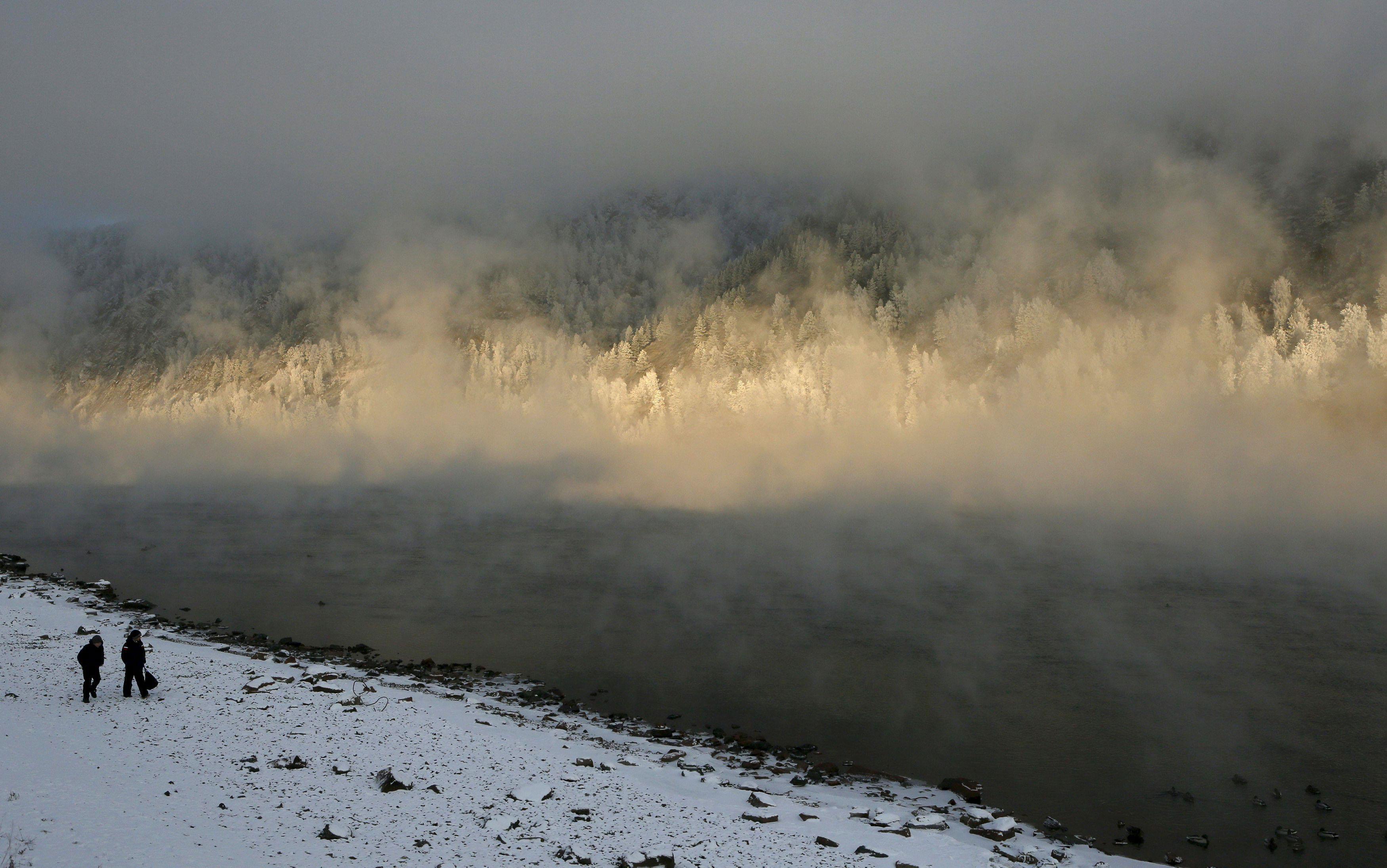 Schoolchildren walk along bank of Yenisei River covered with frosty fog in Divnogorsk near Krasnoyar