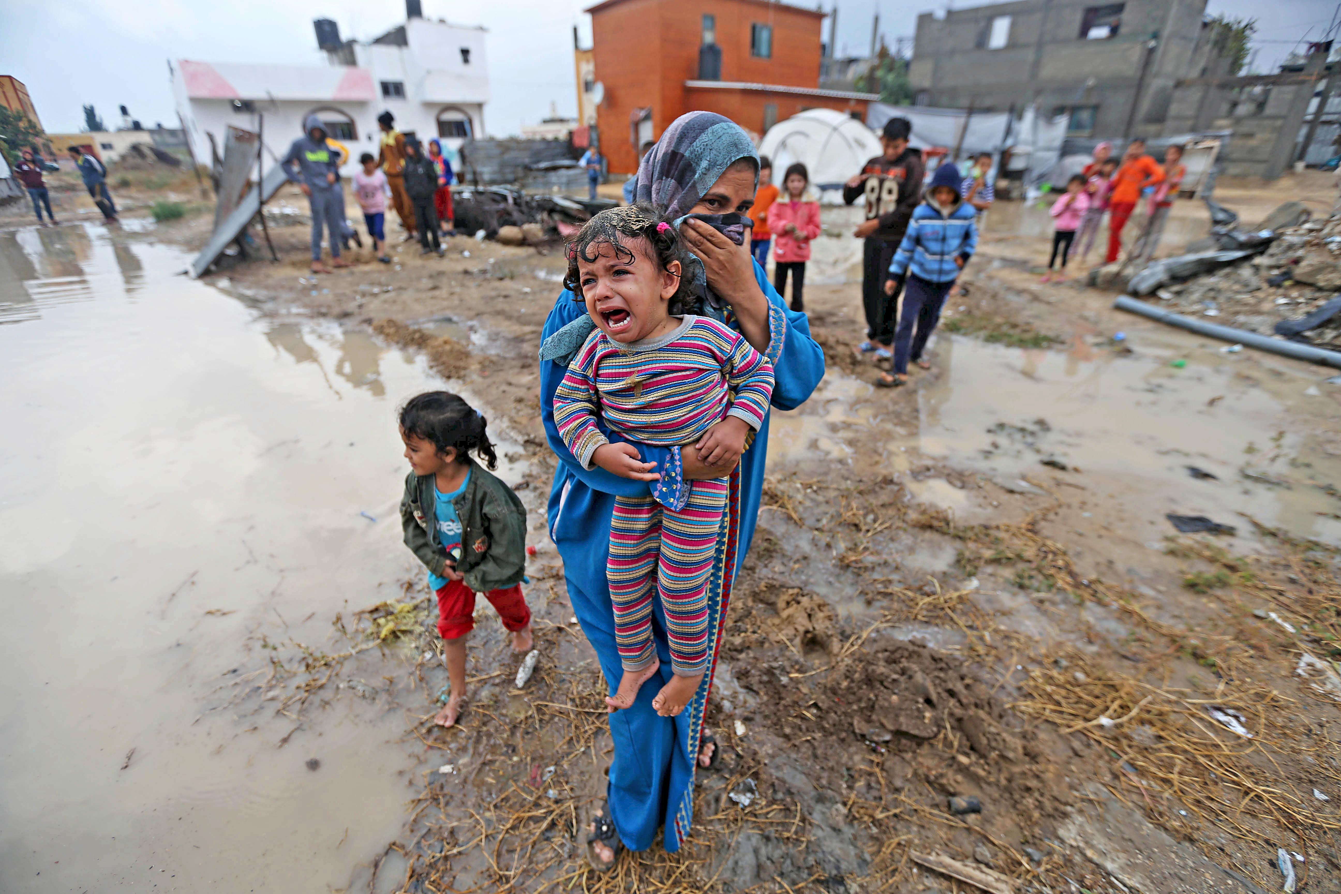 A Palestinian woman carries her crying daughter after rainwater flooded their house in Khan Younis i