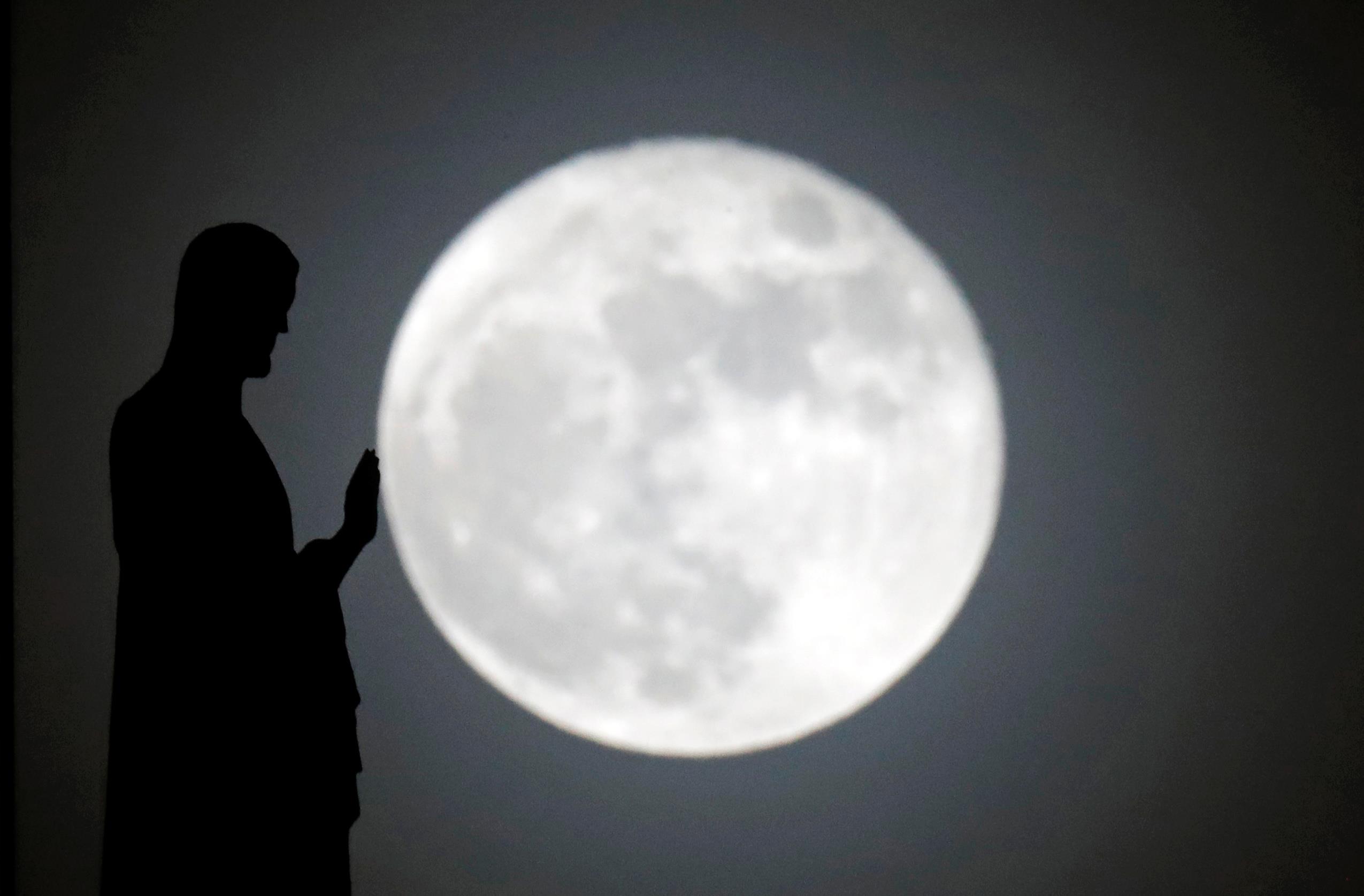 A statue on the roof of Notre-Dame cathedral is silhouetted in front of a supermoon in Paris