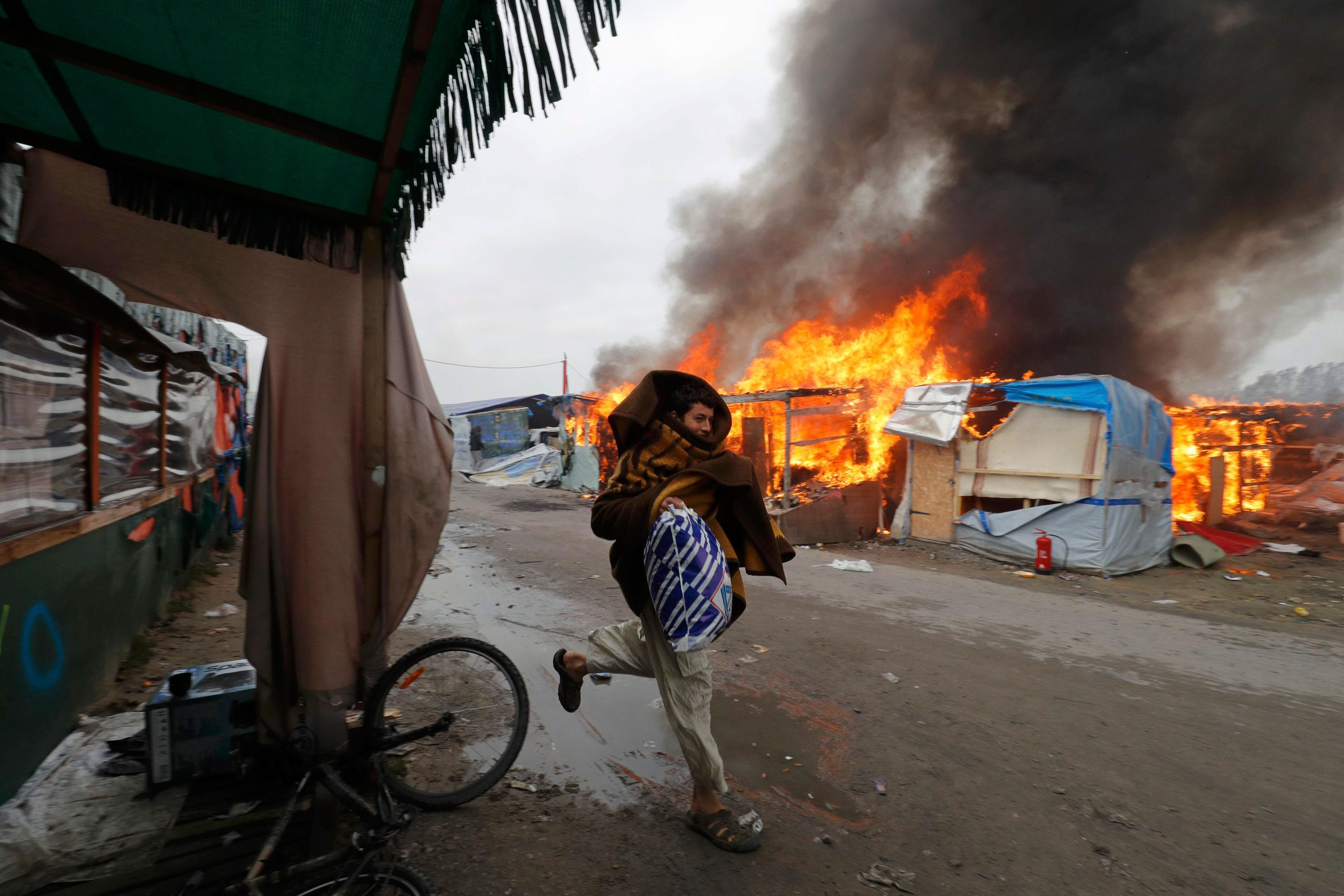 A migrant runs past a burning makeshift shelters in the 