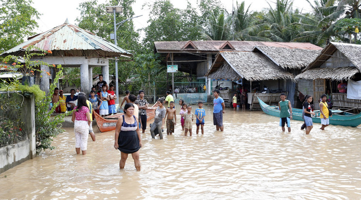 A heves esőzések által megáradt folyó vizében állnak emberek /Fotó: MTI