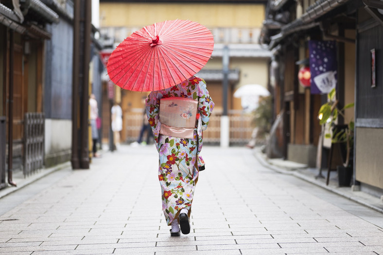 <strong>Antyczne Kioto</strong>
<br></br>
Dawna stolica Japonii Imperialnej (794-1869) przyciąga do siebie niczym magnes. Starożytne świątynie, tradycyjne drewniane domy machiya i delikatne gejsze snujące się po brukowanych uliczkach dzielnicy Gion, wszystko to sprawia, że czujemy się tu tak, jakby ktoś przeniósł nas w czasie. Jeżeli w Japonii pociąga Was tradycja i historia, musicie zobaczyć Kioto.
<br></br>
Miasto jest domem dla niemal 2000 buddyjskich świątyń, doskonale zachowanych przez wieki, których piękno podkreślają bujne japońskie ogrody. Architektura religijna słynnej świątyni Fushimi Inari Taisha, poświęconej bogini Inari, nie ma sobie równych. Przejście przez tysiąc pomarańczowych bram torii prowadzących do shintoistycznej budowli to niezapomniane doznanie duchowe, tym bardziej, że bramy ustawione są wzdłuż ścieżek prowadzących pośród bambusowego lasu. 
<br></br>
Jednak symbolem miasta pozostaje Kinkaku-ji, najpiękniejsza japońska świątynia Zen, zwana Świątynią Złotego Pawilonu. Cała jej fasada pokryta jest płatkami prawdziwego złota. Warto zobaczyć ten widok o zachodzie słońca, gdy rozświetlone ściany błyszczą na tle zieleni. Nic dziwnego, że jest to jeden z najsłynniejszych i najczęściej fotografowanych obiektów w całej Japonii. 
<br></br>
Kultura Kioto zdecydowanie wykracza jednak poza religijną architekturę i artefakty. Jest to miasto, w którym spróbować można najlepszych potraw na świecie. Bez względu na to, czy wybierzemy się na pełną artyzmu ucztę kaiseki (wielodaniowy posiłek, który powstał około 500 lat temu jako akompaniament do ceremonii parzenia herbaty), czy sięgniemy po uliczne specjały, takie jak makaron ramen i tempura – możemy być pewni, że będą to tradycyjne potrawy w najlepszym wydaniu. 
<br></br>
<a  href=