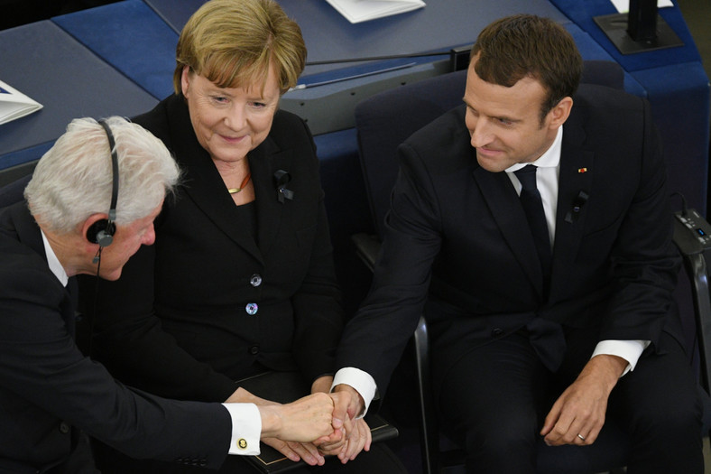 Bill Clinton ściska dłoń Emmanuela Macrona, między nimi Angela Merkel