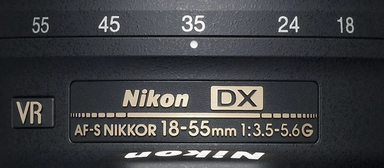 Oznaczenie zakresu ogniskowych na obudowie obiektywu Nikkor. Ponieważ jest to obiektyw przeznaczony dla lustrzanek niepełnoklatkowych (APS-C - w przypadku lustrzanek Nikon mówi się o matrycy DX), by uzyskać informacje o efektywnym polu widzenia tego obiektywu, należy pomnożyć wartości ogniskowych przez przelicznik ogniskowych (w tym przypadku 1,5 - matryca DX ma o tyle mniejszą przekątną od przekątnej pełnej klatki). Obiektyw ten oferuje ekwiwalent ogniskowych 27-82,5 mm