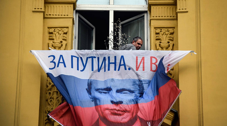 Putyin képével ellátott transzparenst függeszt ki egy férfi a választási kampány részeként / Fotó: AFP