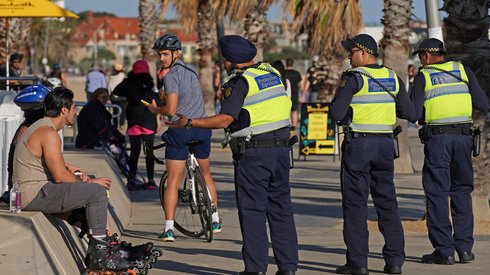 Funkcjonariusze służb ochronnych Victoria Police rozmawiają z mężczyzną na plaży St Kilda w Melbourne. Zamknięto nieistotne usługi w całej Australii w celu spowolnienia rozprzestrzeniania się choroby COVID-19. Fot. PAP/EPA/Scott Barbour