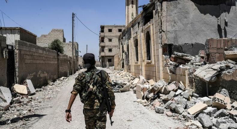 A member of the Syrian Democratic Forces (SDF), an alliance of Kurdish and Arab fighters, walks on a damaged street in western Raqa