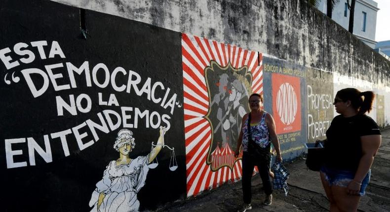 People walk past murals protesting the state of the economy in San Juan, Puerto Rico, as the former Spanish colony of 3.5 million, now a US territory, struggles under a mountain of debt