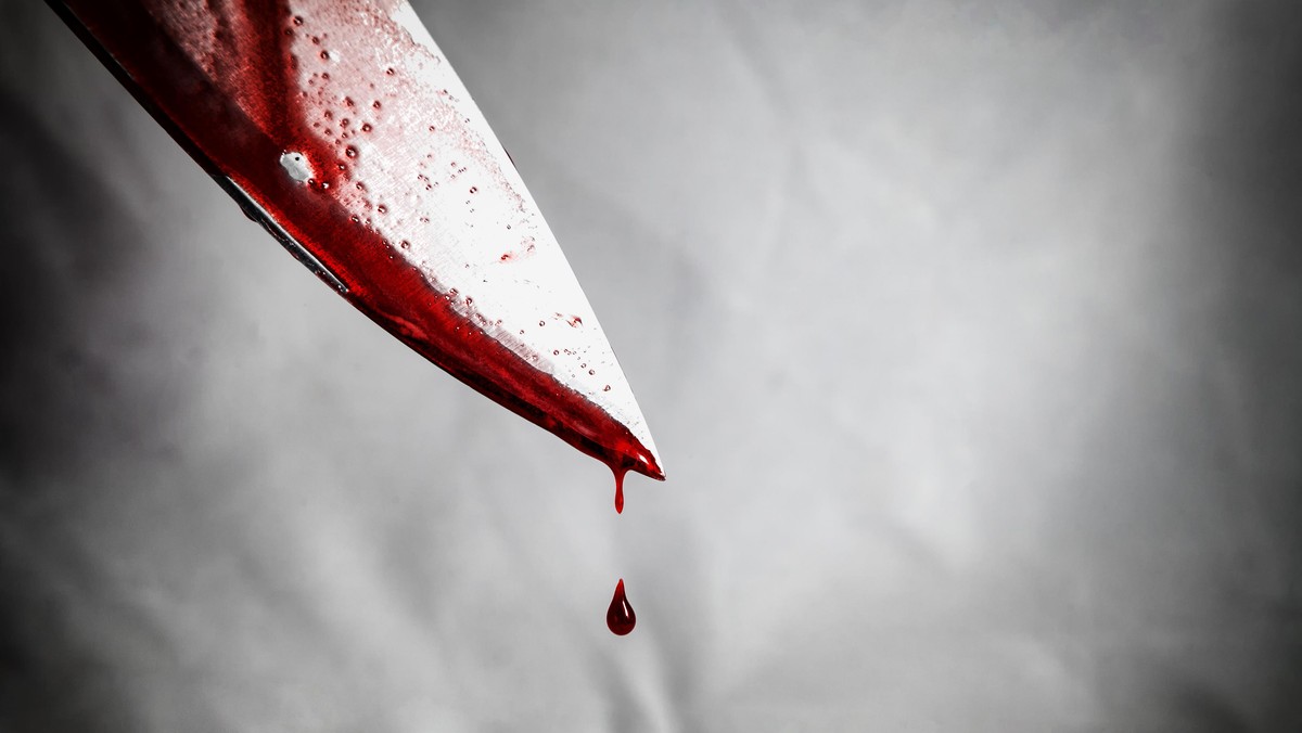 close-up of man holding knife smeared with blood and still dripping.