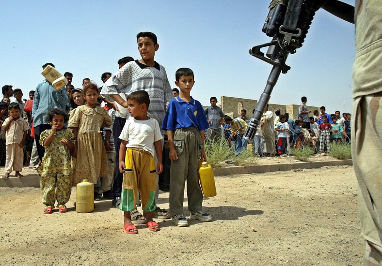Żołnierz amerykański stoi na straży przed irackimi dziećmi czekającymi na benzynę w Faludży w Iraku, 15 czerwca 2003 r.