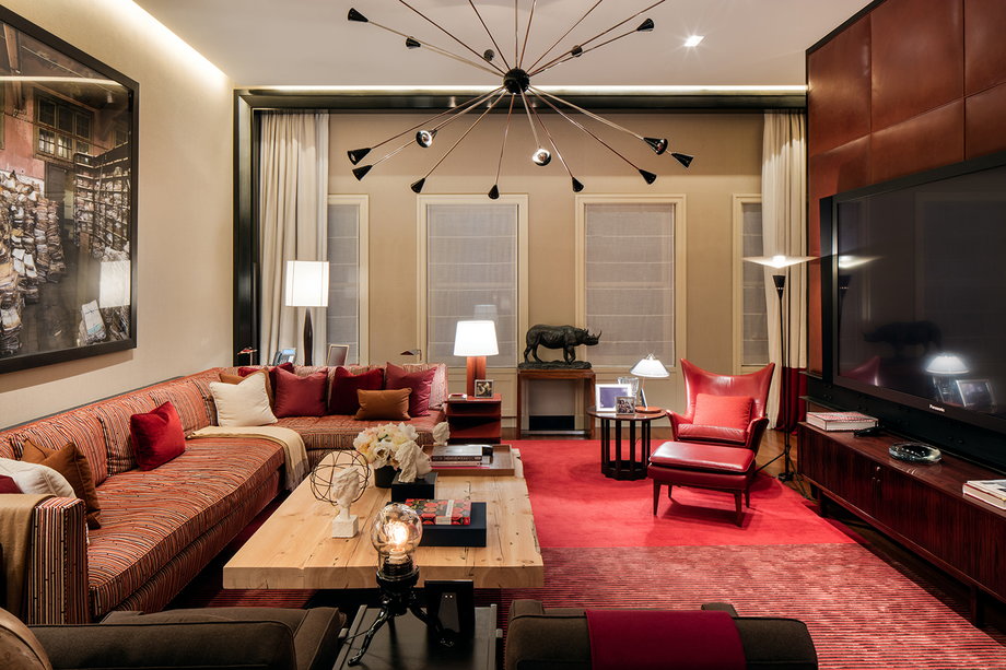 A high-ceilinged living room boasts a leather-paneled wall and warm red accents.