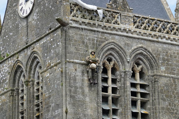 Nietypowe upamiętnienie. Figura alianckiego spadochroniarza znajdująca się na kościele w Sainte-Mère-Église (fot. PsamatheM, opublikowano na licencji Creative Commons Uznanie autorstwa-Na tych samych warunkach 4.0 Międzynarodowe).