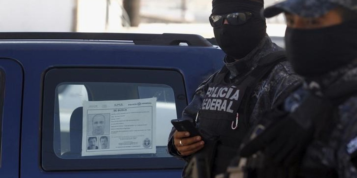 Mexican federal-police officers stand guard near a vehicle with a "Wanted" sign for then fugitive kingpin Joaquin "El Chapo" Guzman glued to the window, in Tijuana, October 24, 2015.