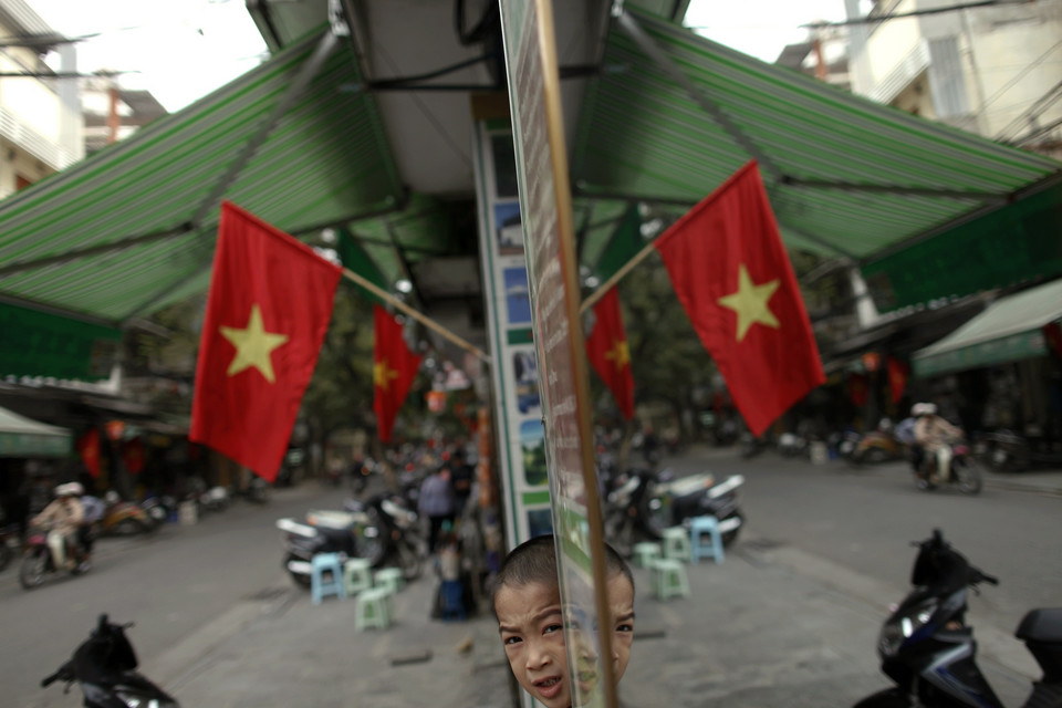 A Vietnamese boy is reflected in a mirror along a street decorated with national flags, in downtown Hanoi