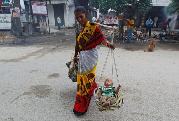 A woman carries her child in a basket as she walks on a road in Allahabad