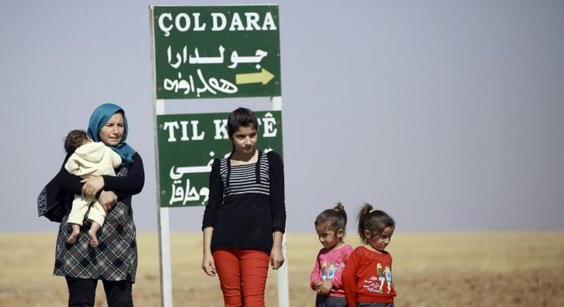 A Kurdish woman and her children stand by a sign for the village of Joldara (meaning plain covered in trees) and known as Shajra in Arabic, near the northeastern Syrian city of Qamishli on October 3, 2016