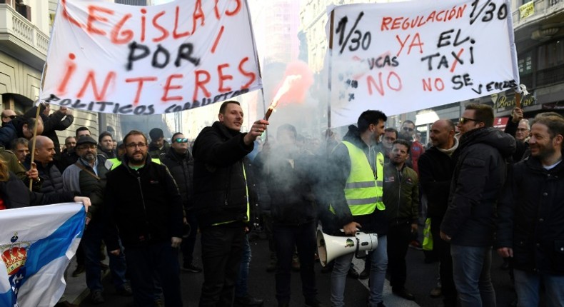 Taxi drivers hold flares and placards reading Regulation now during a demonstration in to protest against online ride-sharing services like Uber