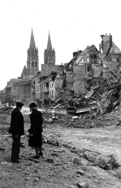 Para mieszkańców Caen obserwuje kanadyjski buldożer oczyszczający drogę. W tle widoczne Abbaye aux Hommes (Opactwo Męskie) (10 lipca 1944, domena publiczna).