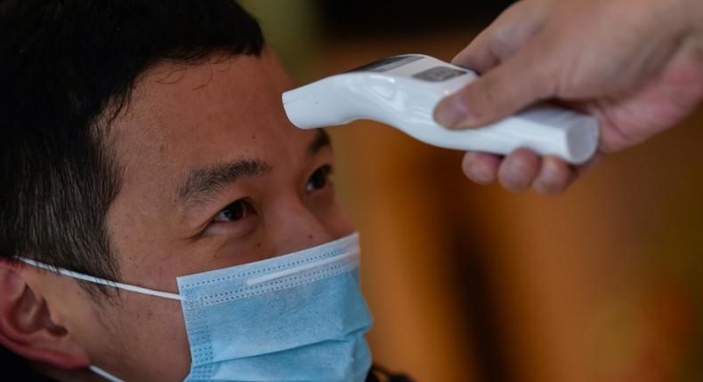 A hotel employee takes the temperature of a man who just arrived in the building in Wuhan