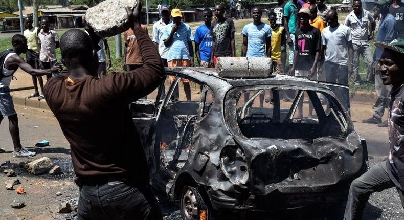 A man throws a stone on a burnt car as supporters of Kenya's opposition party National Super Alliance (NASA) demonstrate in Kisumu, on November 20, 2017 after Kenya's Supreme Court dismissed two petitions to overturn the country's October 26 presidential election re-run, validating the poll victory of Kenyatta. (Photo by BRIAN ONGORO/AFP via Getty Images)